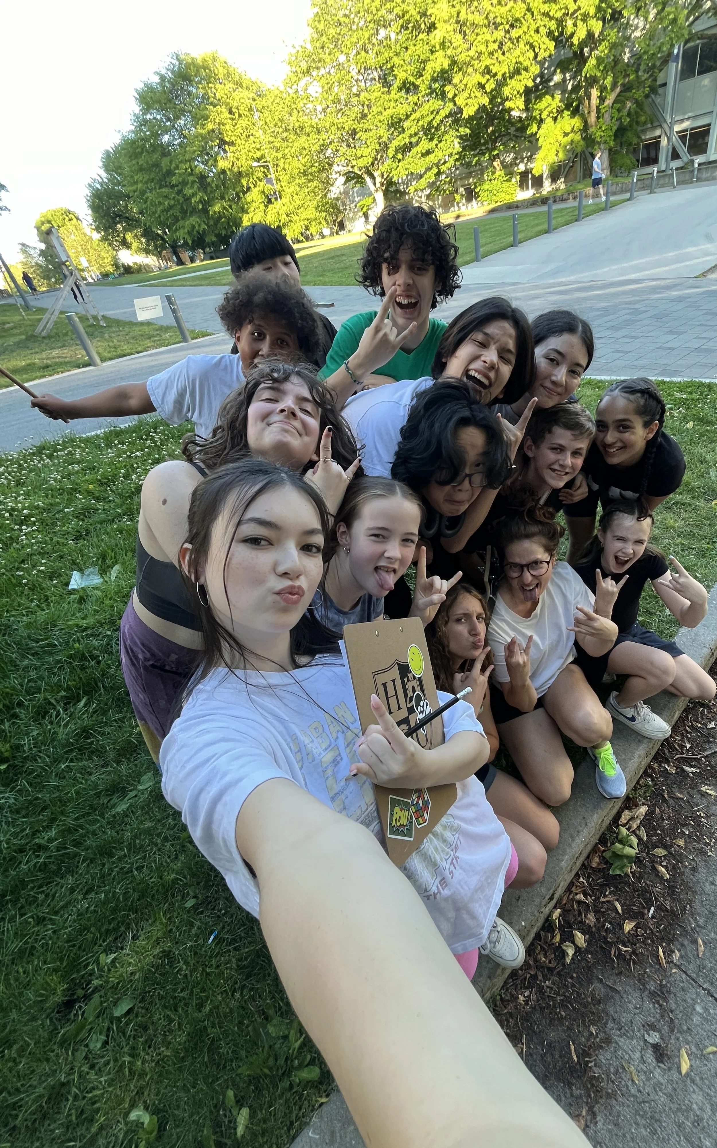 Group of young friends taking a selfie outdoors in a park, smiling and making playful gestures.