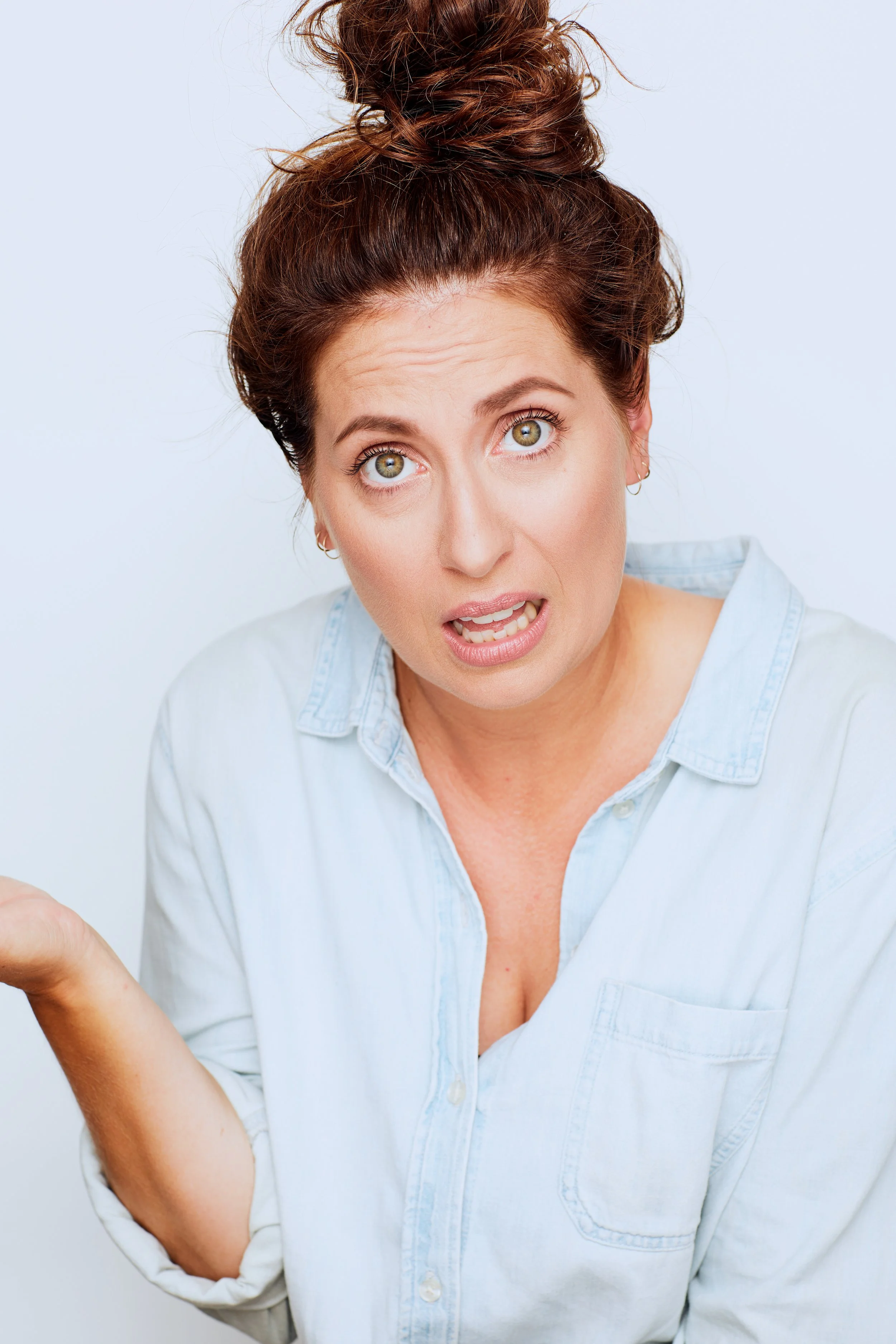 A woman with a surprised or confused expression, with her mouth slightly open and eyebrows raised, wearing a light blue shirt.