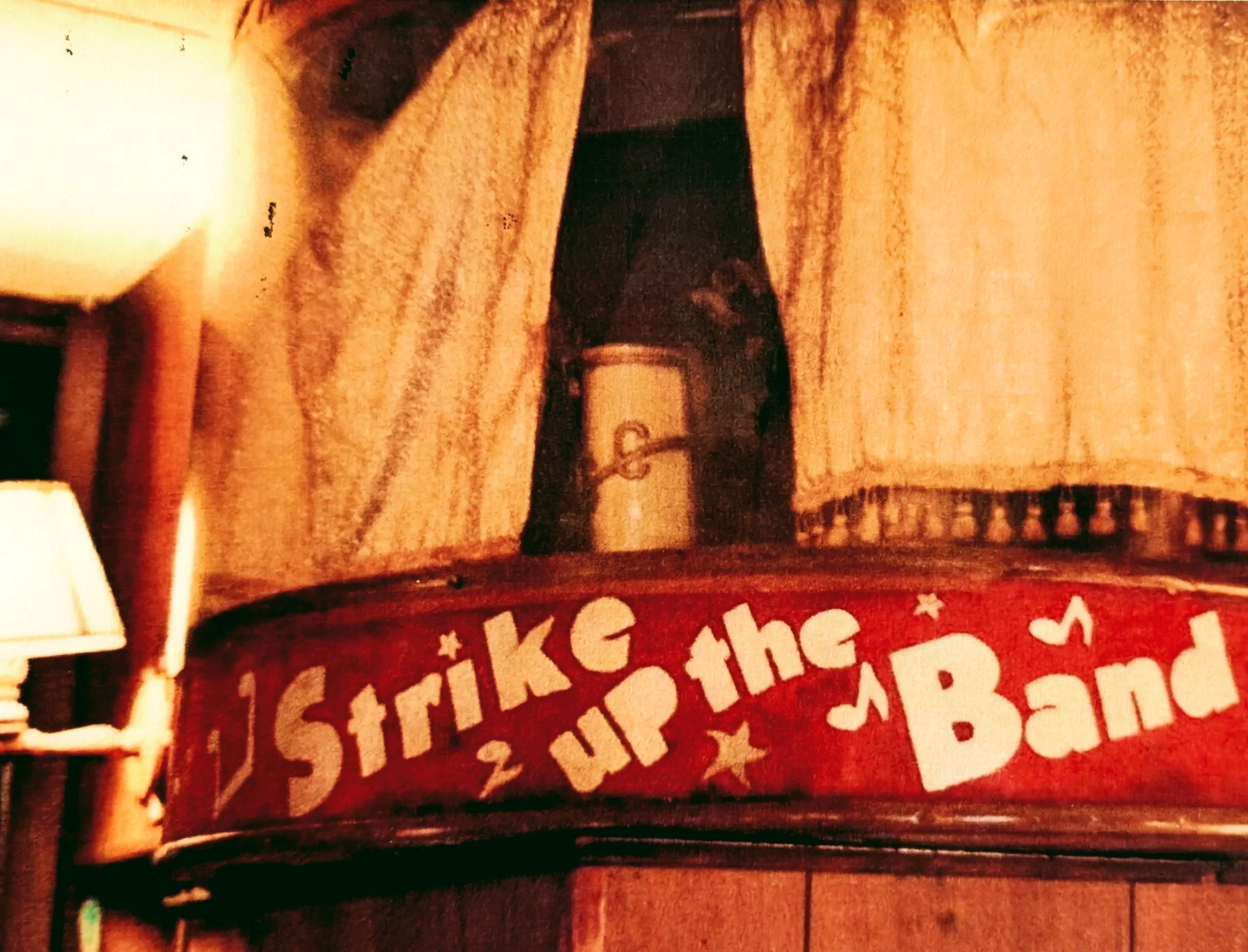 A red drum with white letters decorated with stars that reads "Strike up the Band" located on a wooden surface.