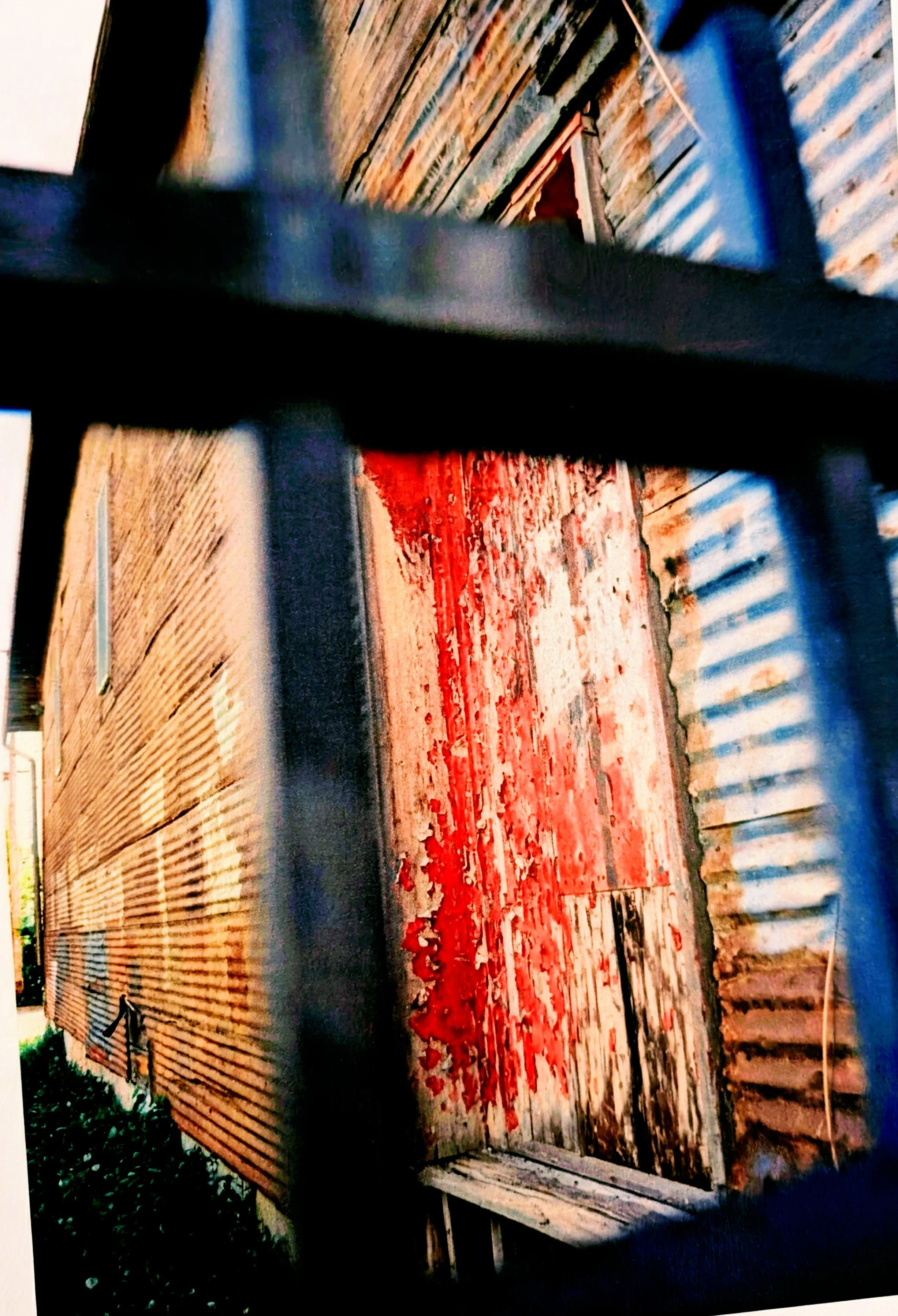 A rustic wooden barn with a weathered red door, seen through black metal bars.