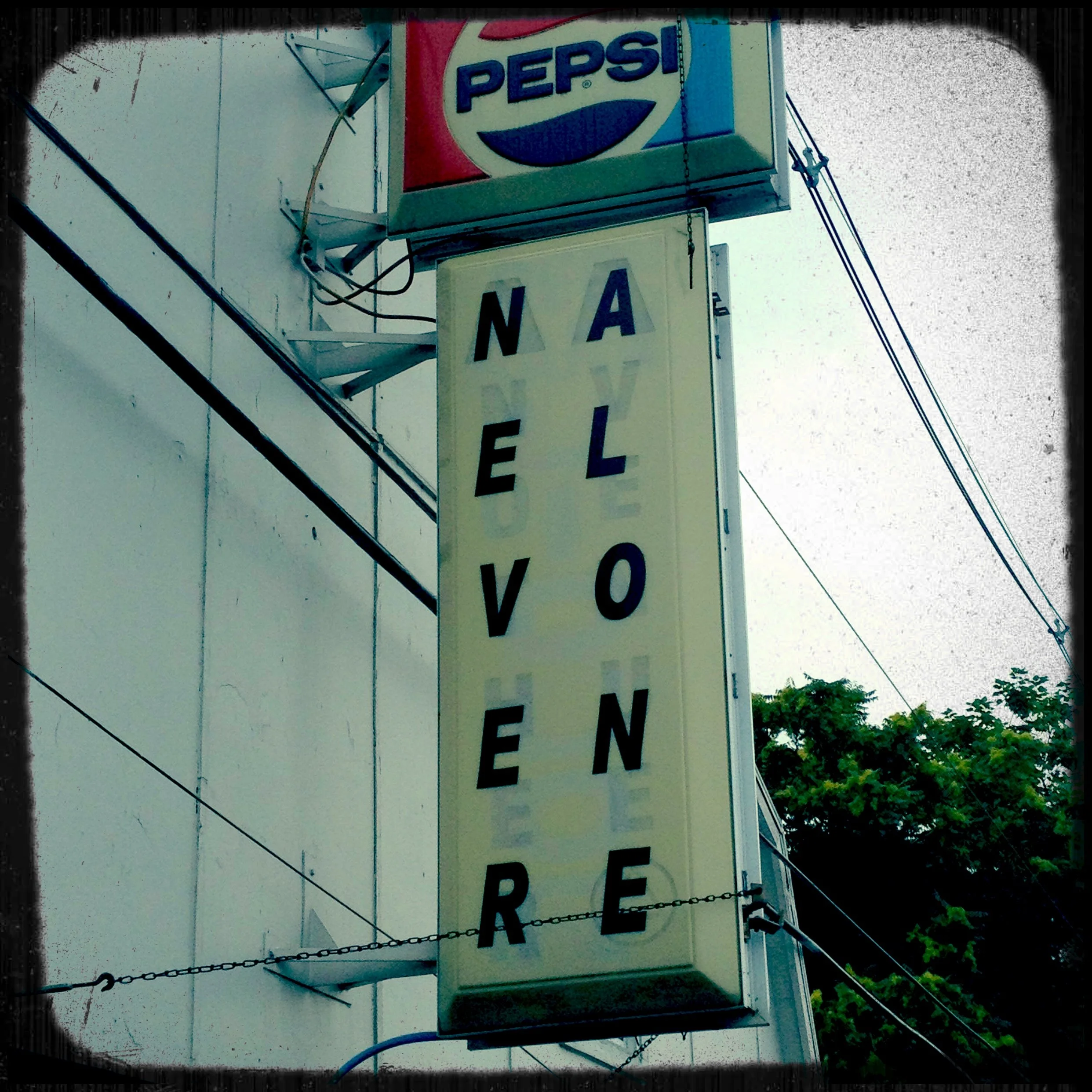 A vertical neon sign on a building reads 'NAVELOVENDER' vertically with black letters on a white background, and a Pepsi advertising sign is positioned above it.