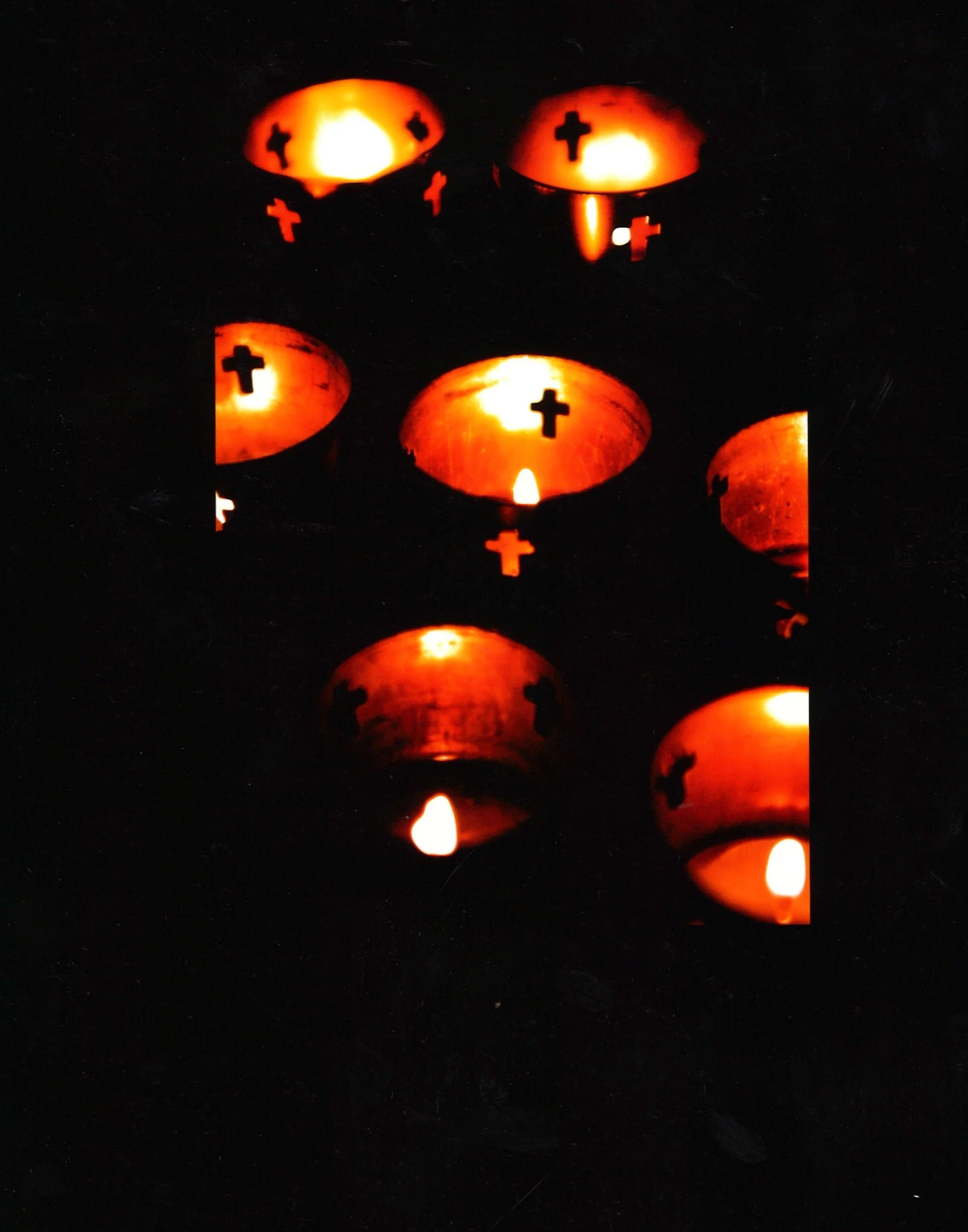 Multiple lit pumpkin jack-o'-lanterns with cross-shaped cutouts, arranged on a dark background, glowing from within.