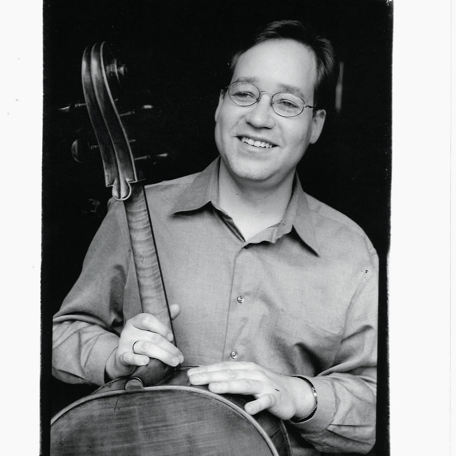 Black and white photo of a young man with glasses smiling, holding a trophy and resting his hand on a drum.