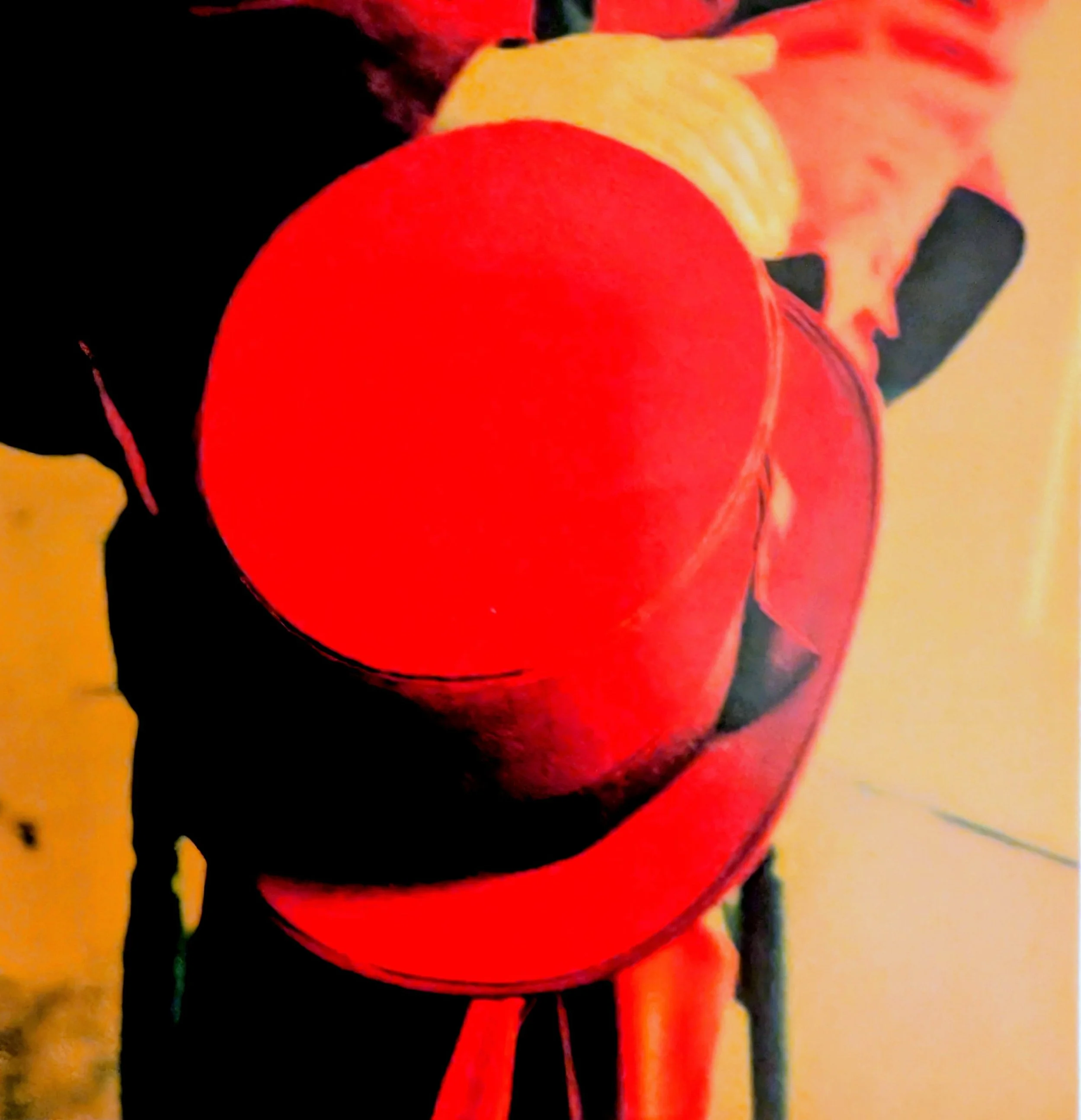 A close-up of a person holding a large red balloon with one hand, standing indoors near a wall.