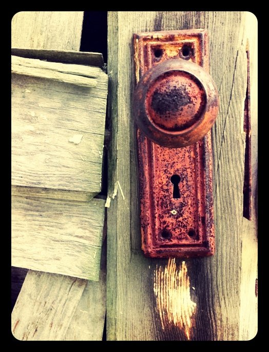 Close-up of an old, rusty door knob and keyhole on a weathered wooden door.