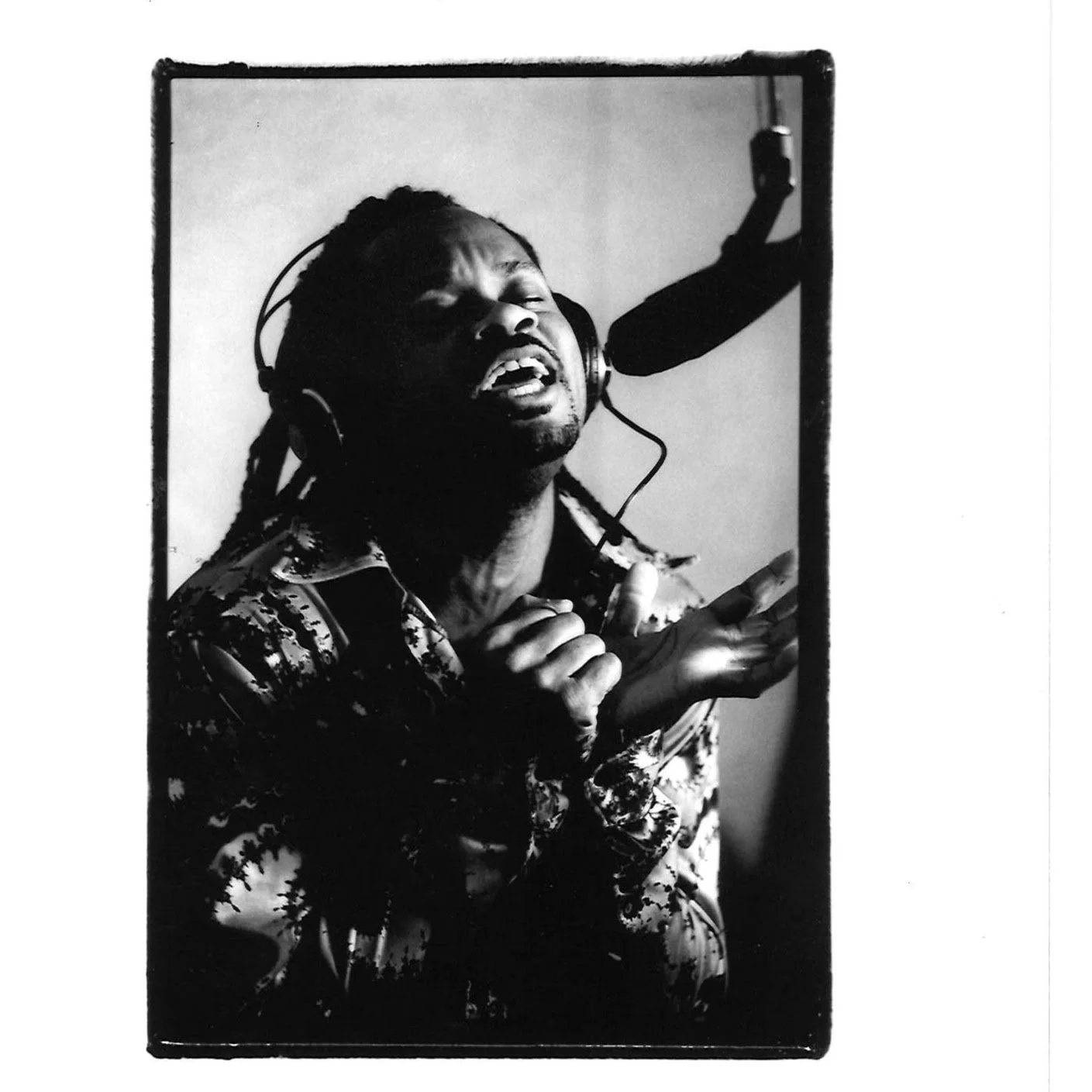 Black and white photo of a male singer with headphones, singing passionately into a microphone in a recording studio.