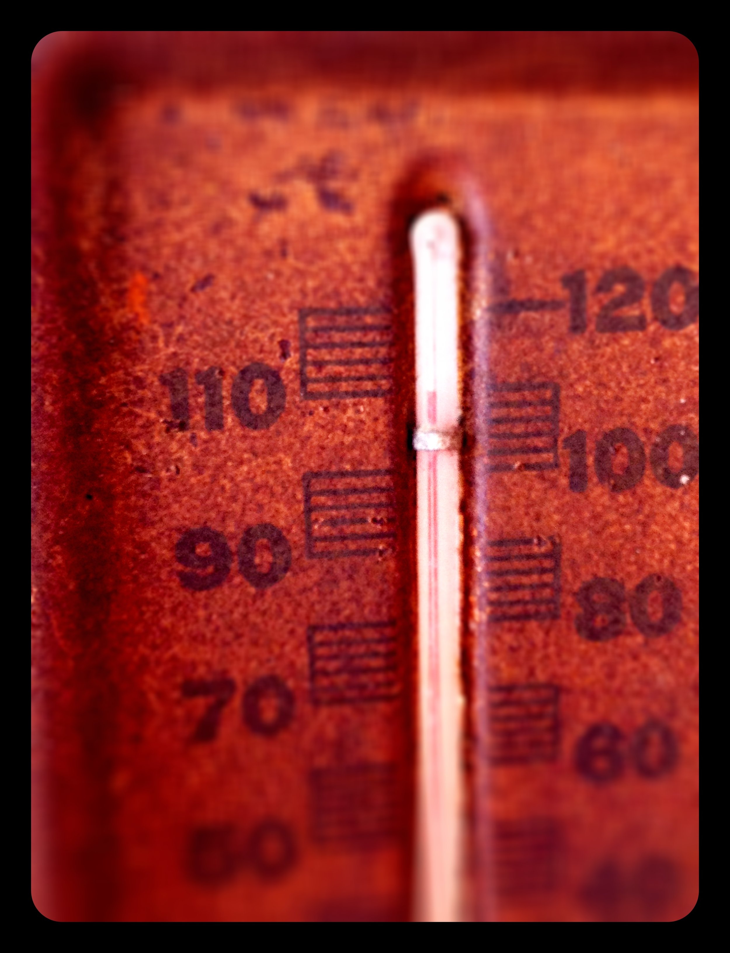 Close-up of a rusty red-colored surface with a vertical glass thermometer embedded in it, displaying temperature measurements.