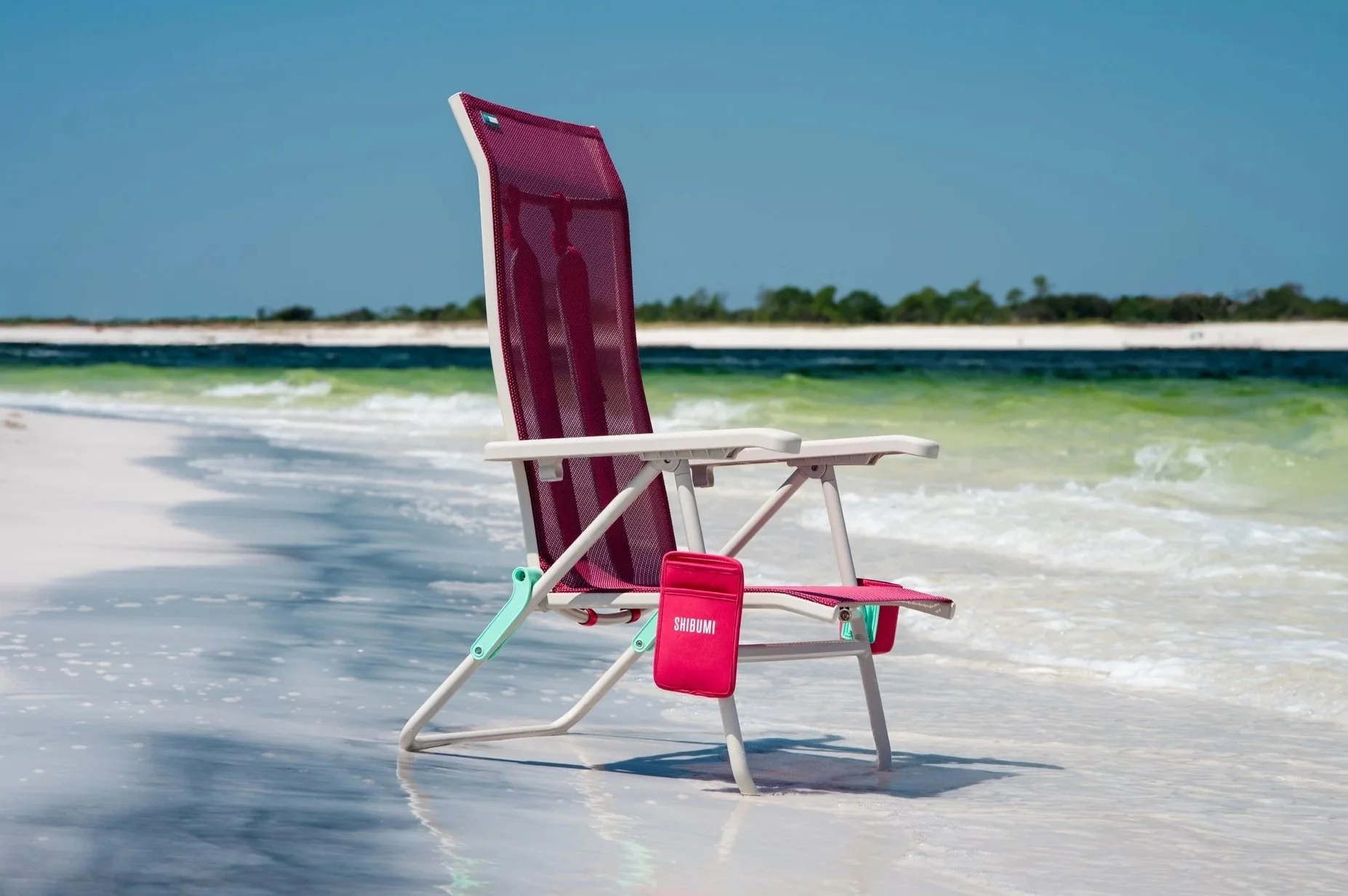 A pink and white beach chair on the sandy shore of a beach with the ocean and distant land in the background.