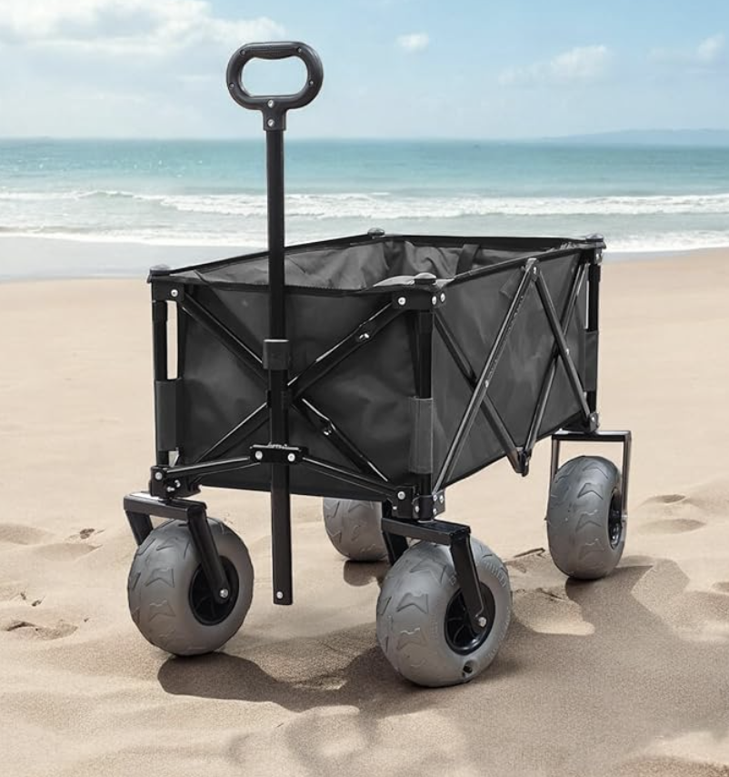 A collapsible utility wagon with large wheels on a sandy beach, background of ocean and blue sky.