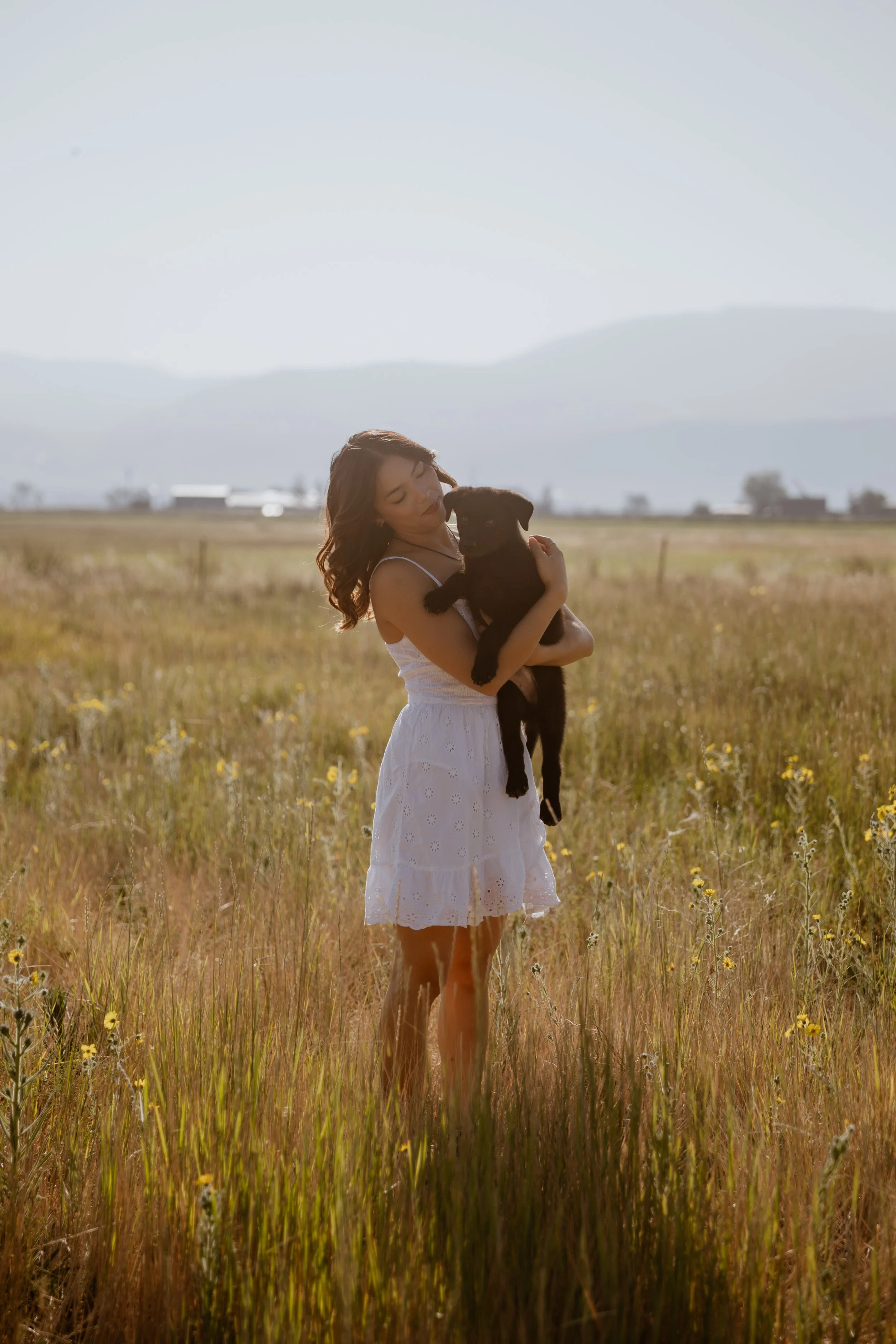 Black and white photo of a woman standing outdoors with trees in the background, wearing a cable-knit sweater and dark pants, looking at the camera with a slight smile.