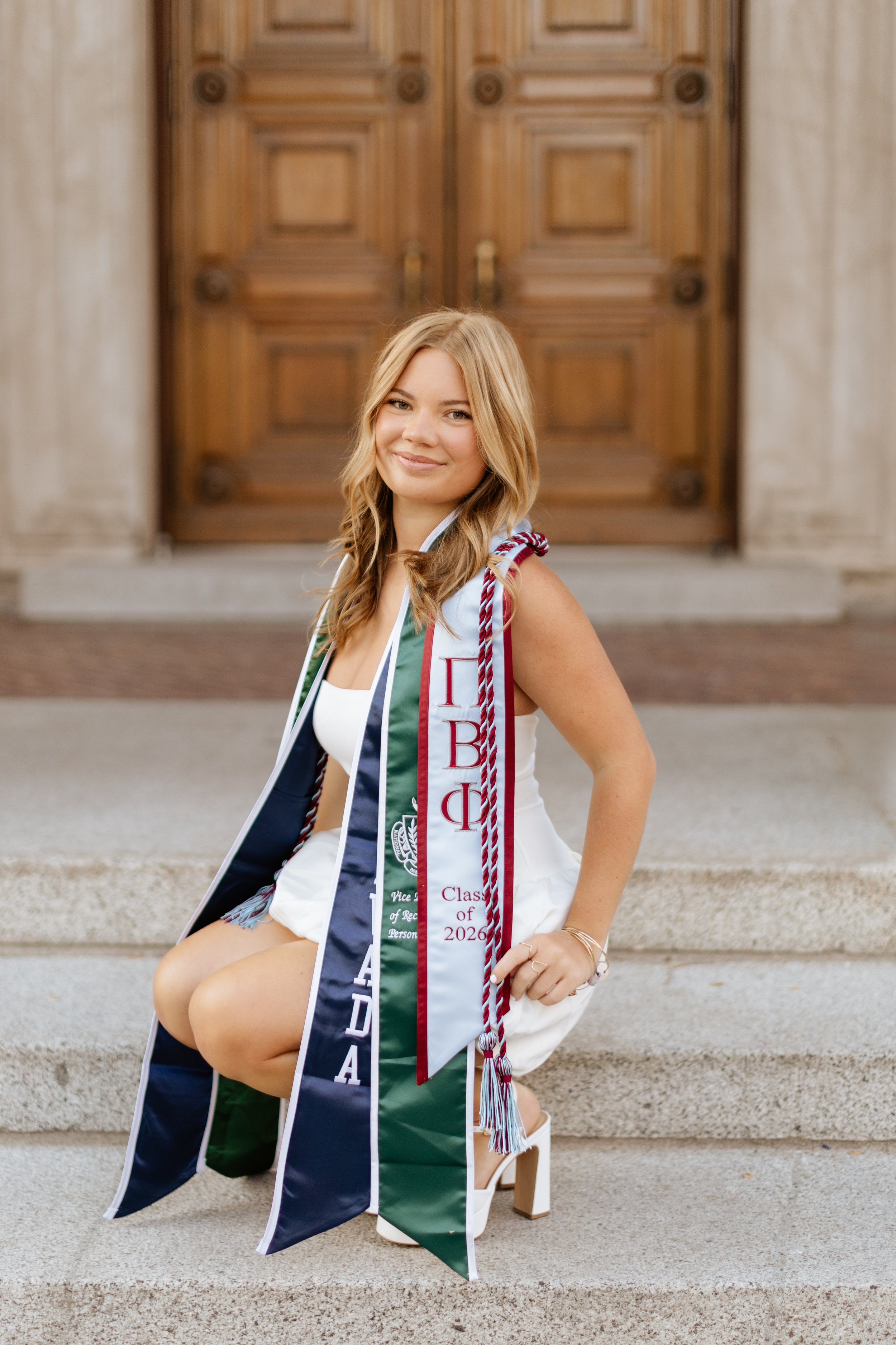 college graduate crouching down in front of Mackay science and showing off her stoles from the university of Nevada Reno