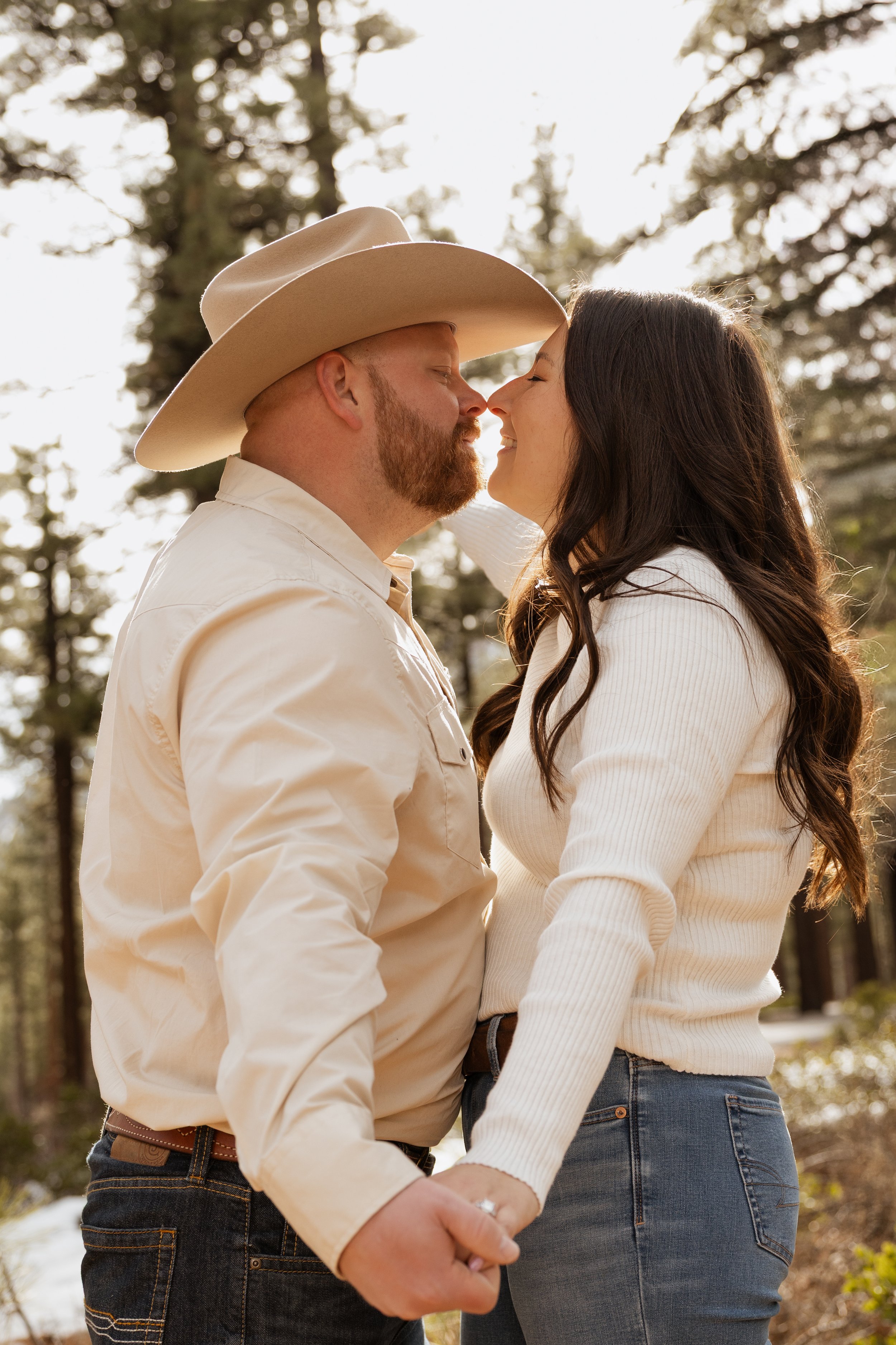 A smiling woman and a man wearing a cowboy hat walk together outdoors in a grassy field with trees in the background.
