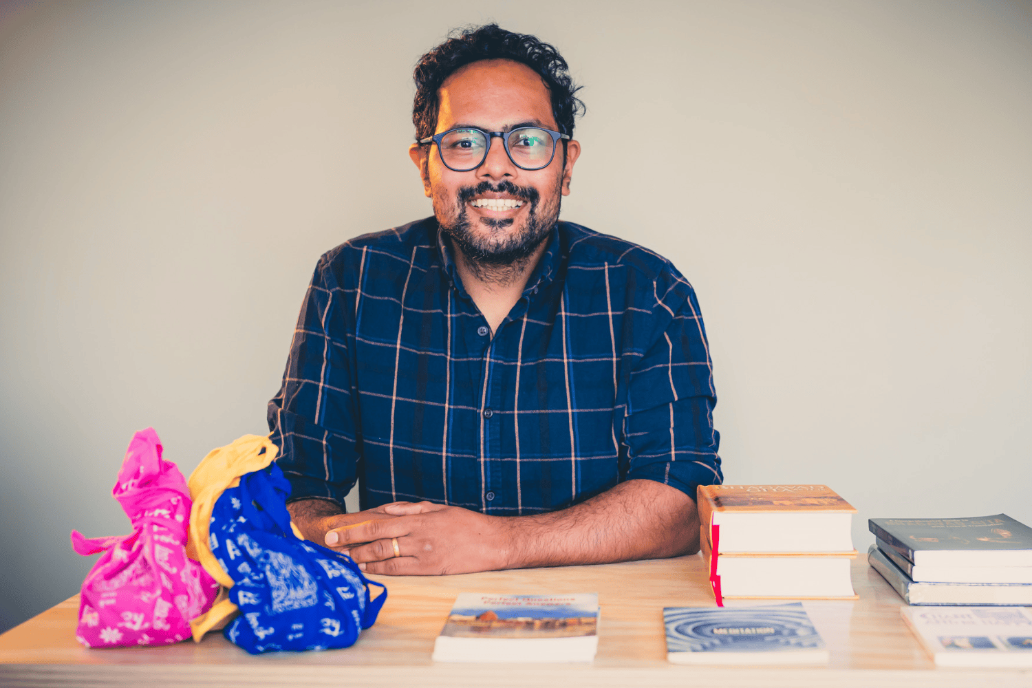 Man smiling at a table with colorful fabric, books, and magazines.