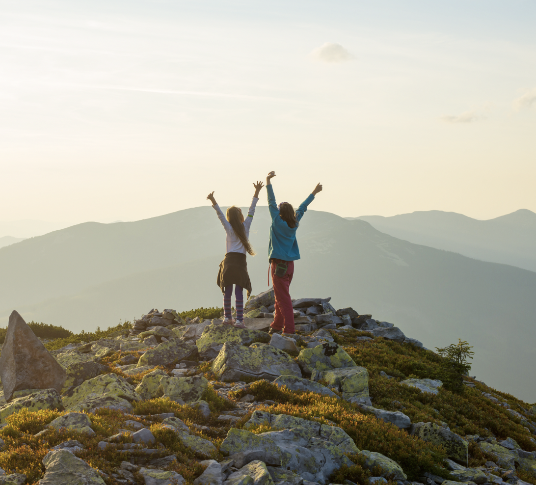 Two teen girls hiking with arms in the air in joy
