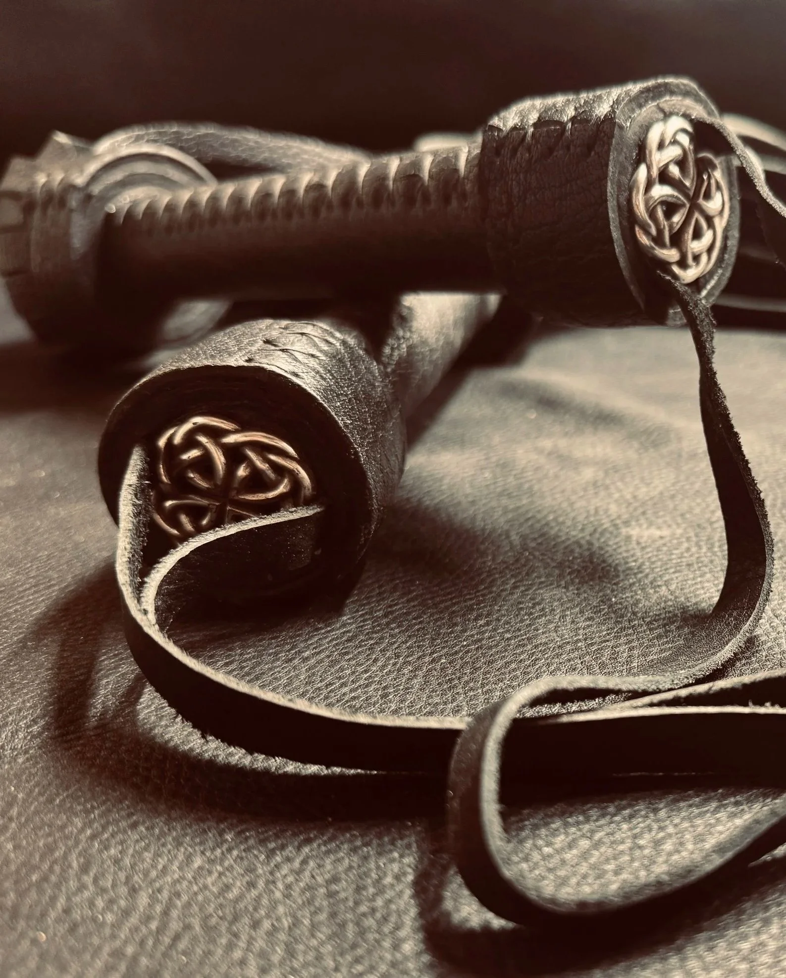 Close-up of a leather-bound object with metal ends engraved with Celtic knot designs, lying on a textured surface.