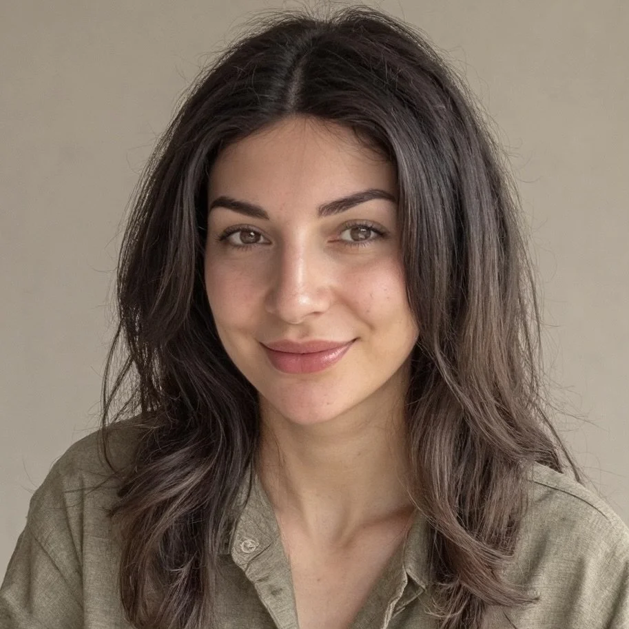 Un portrait d'une femme avec des cheveux bruns ondulés, souriant, portant une chemise beige clair.