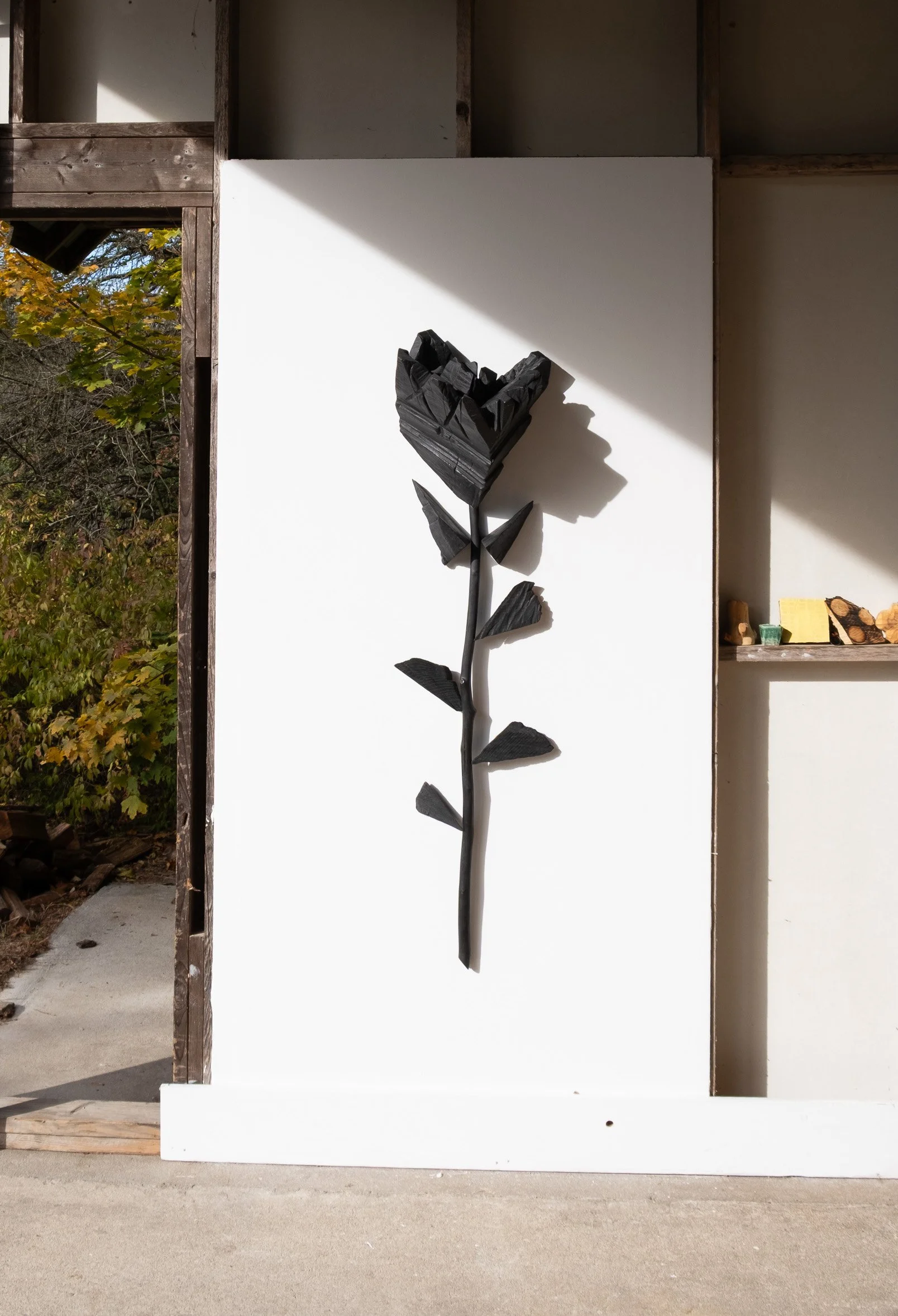 Black wooden flower sculpture mounted on a white wall inside a building.