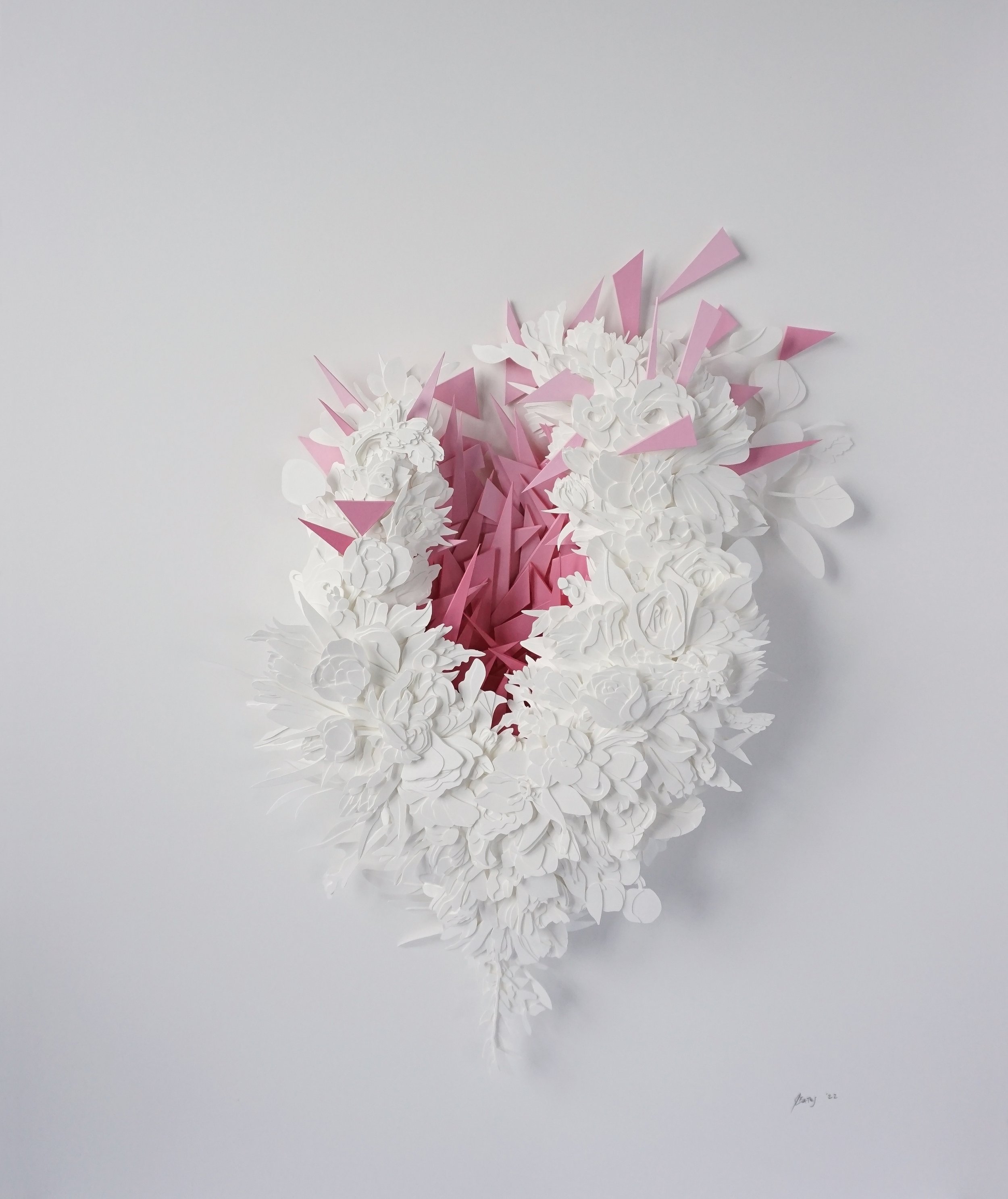 Abstract sculpture with white and pink paper elements arranged in a heart shape on a white background.