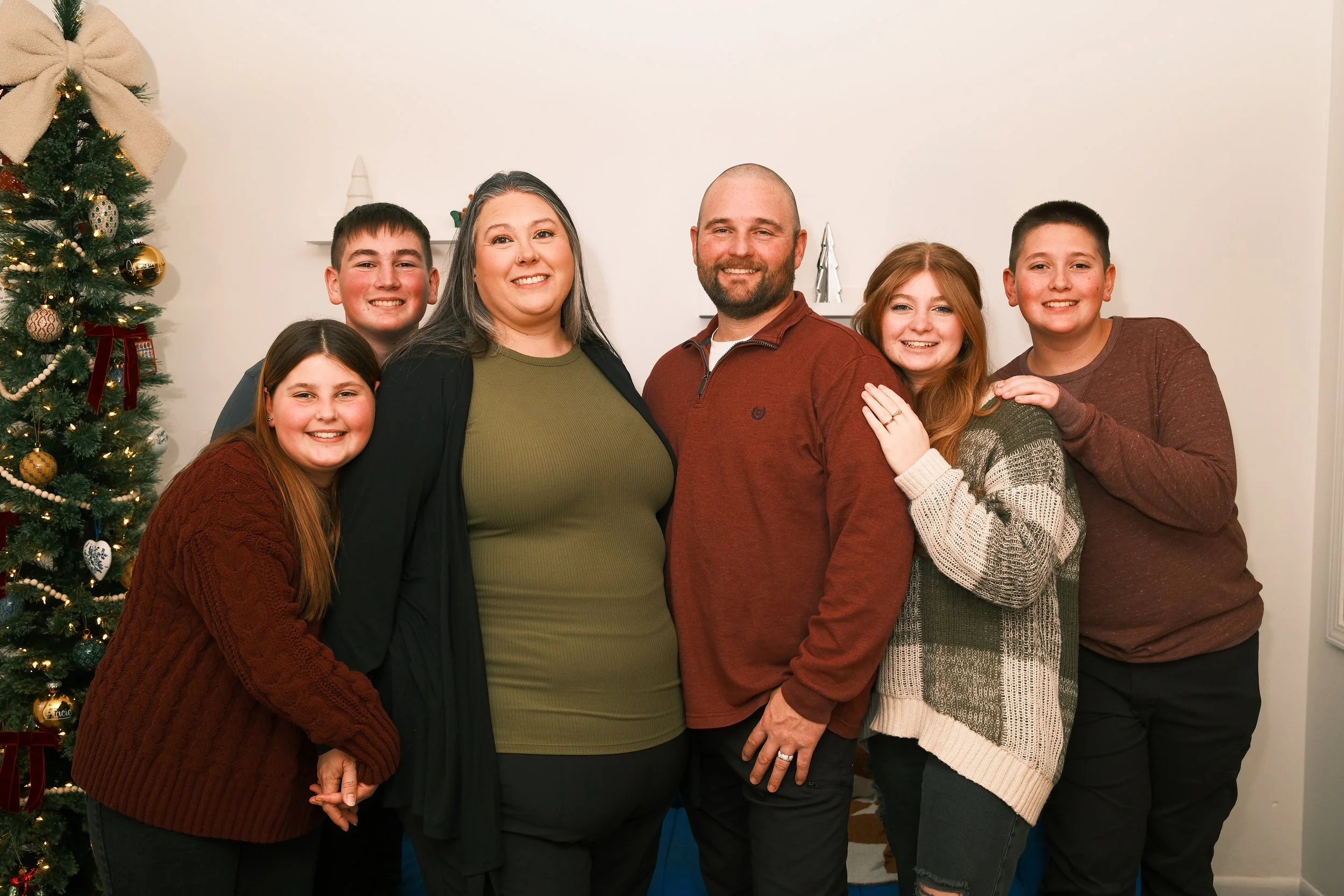 A family of six celebrating Christmas indoors next to a decorated Christmas tree.