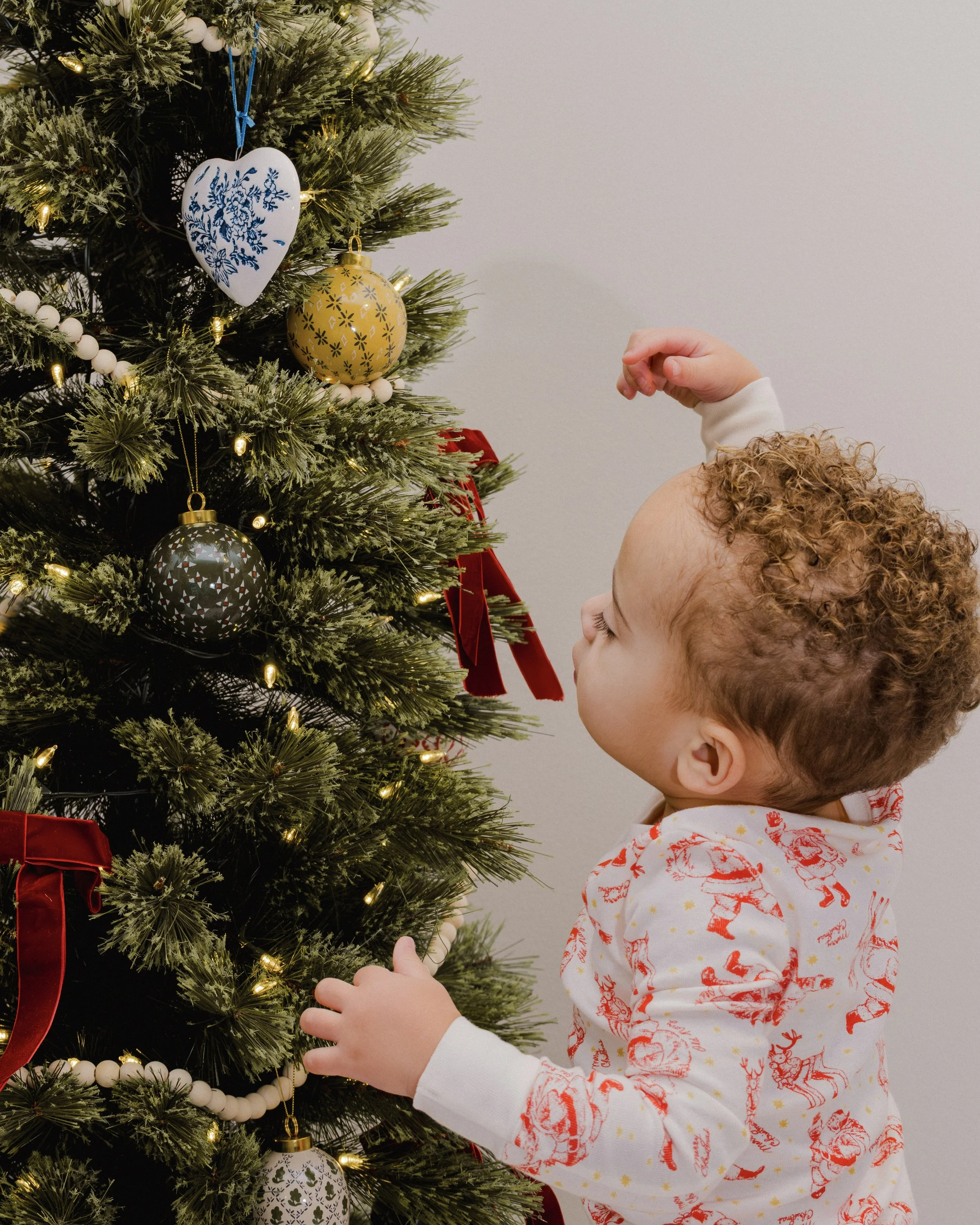 A young child with curly hair decorating a Christmas tree with ornaments and lights.