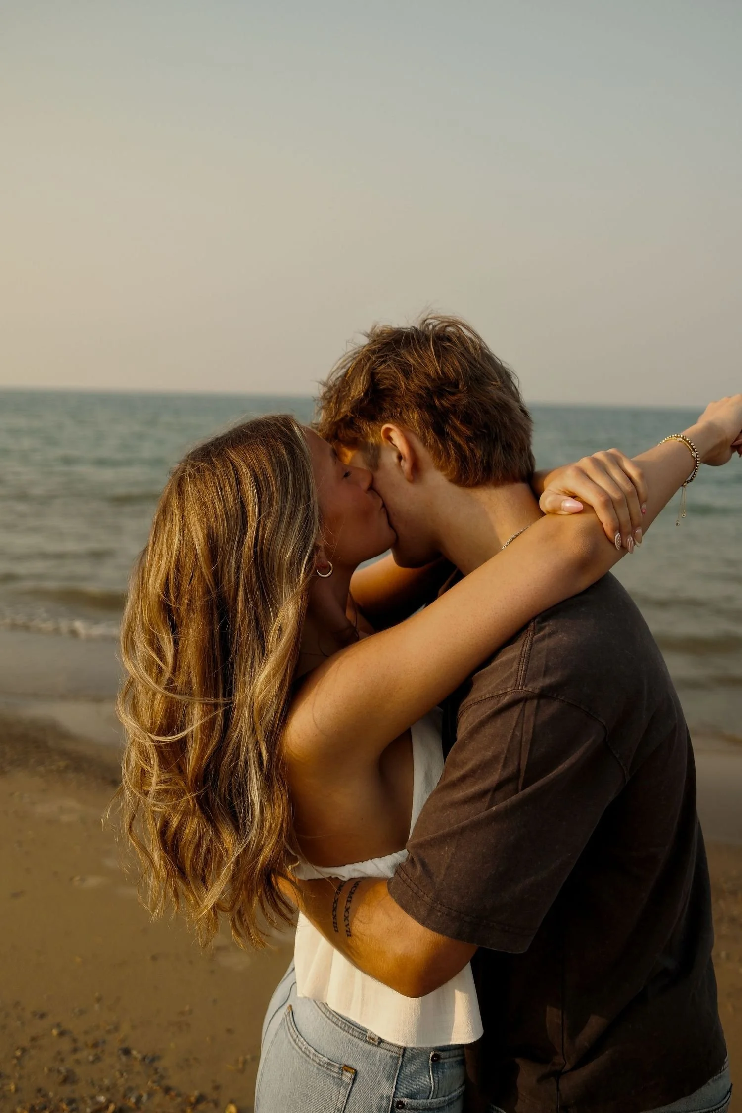 A couple kissing on a beach at sunset, with the ocean in the background.