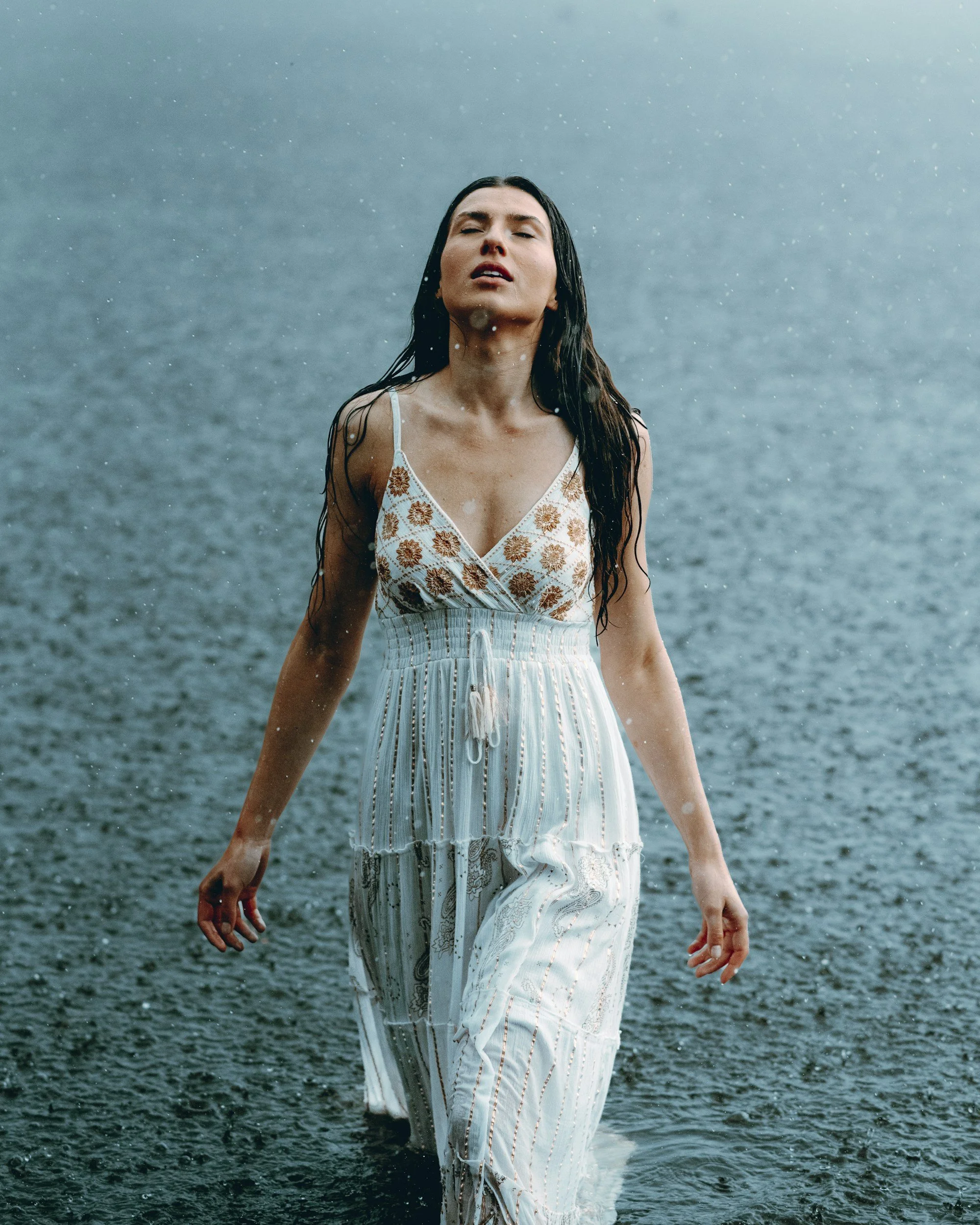 Woman in a white, floral-patterned dress standing in the water, with water splashing around her.