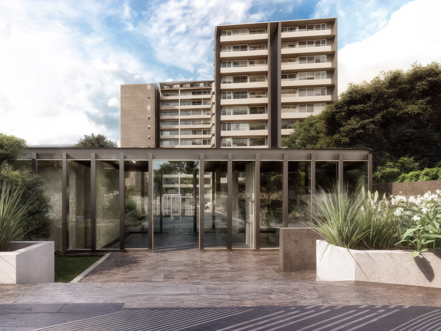 Modern residential building with glass entrance and lush greenery around, under partly cloudy sky.
