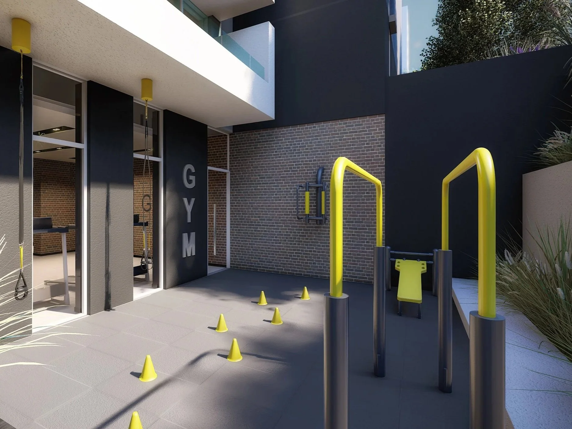 Outdoor gym area with yellow and black exercise equipment, small yellow cones on the ground, and a brick wall on the right side. Glass doors leading inside are on the left, with the word "GYM" vertically displayed.