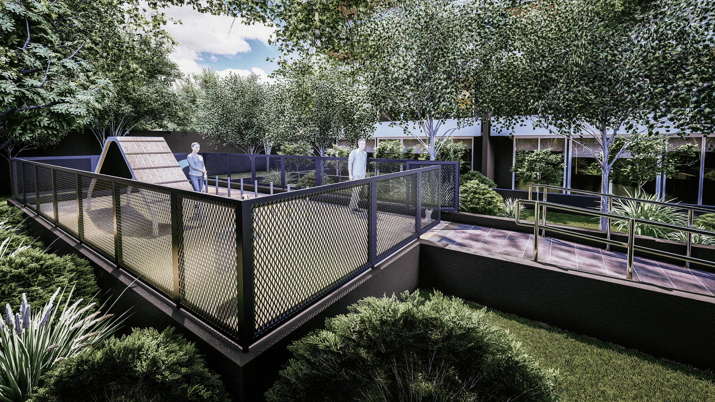 A landscaped outdoor area with a fenced patio, trees, bushes, and a walking path, with two people standing on the patio.