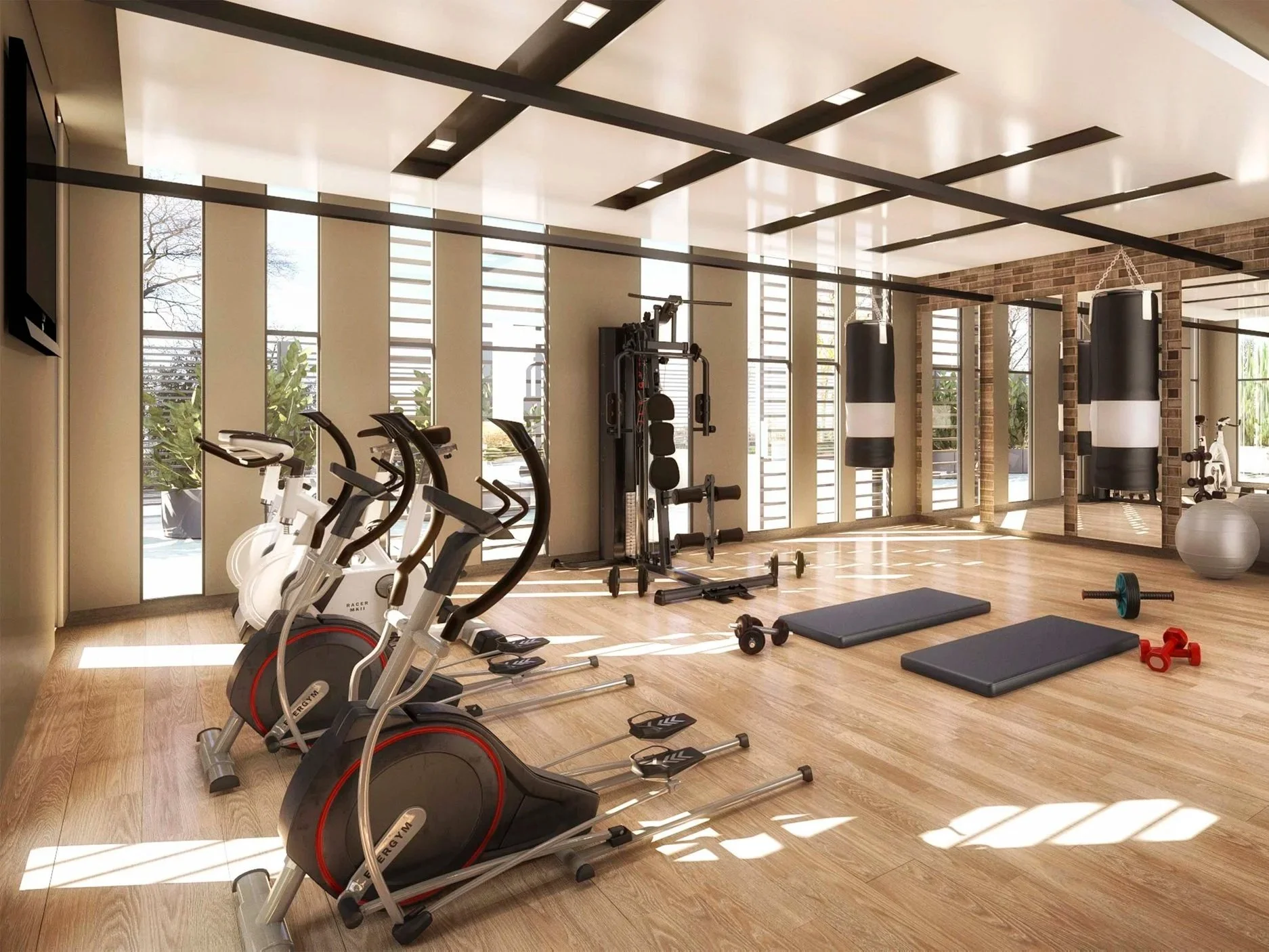 A modern gym with exercise bikes, punching bags, exercise mats, dumbbells, a stability ball, and large windows letting in natural light.