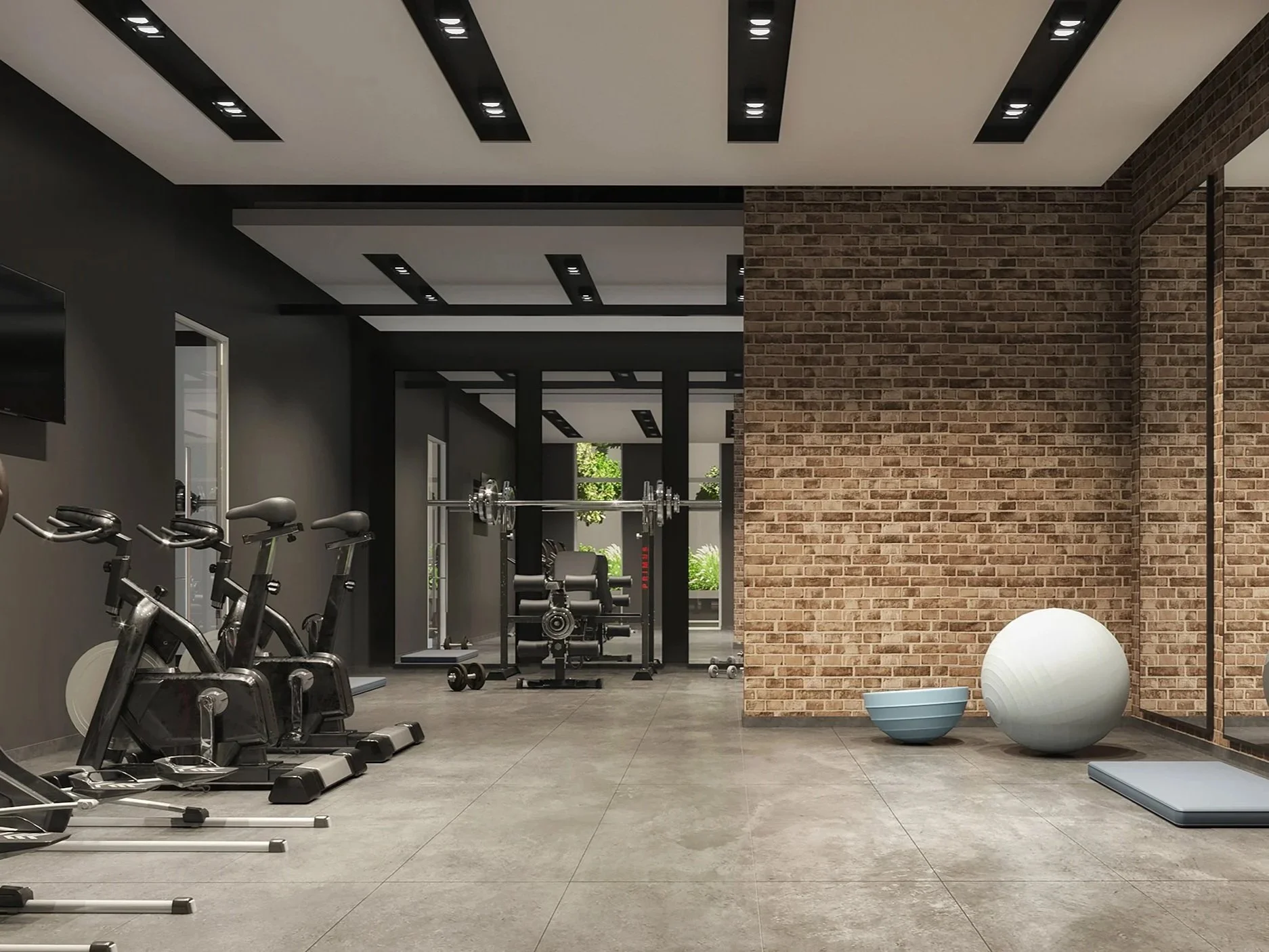 Gym with stationary bikes on the left, weightlifting equipment in the background, and a brick wall with exercise balls and a mat on the right.