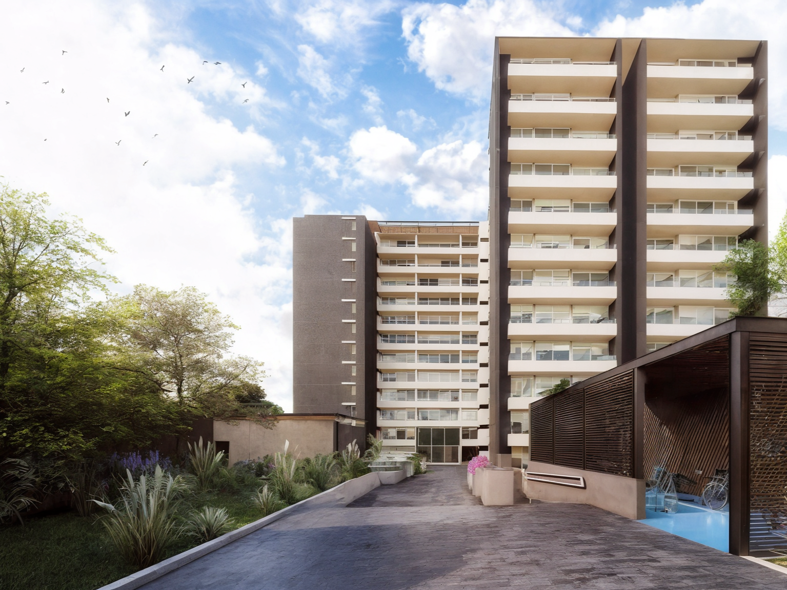 Modern multi-story residential building with balconies, surrounded by greenery and outdoor amenities including seating area and bicycle storage, under a blue sky with clouds and birds