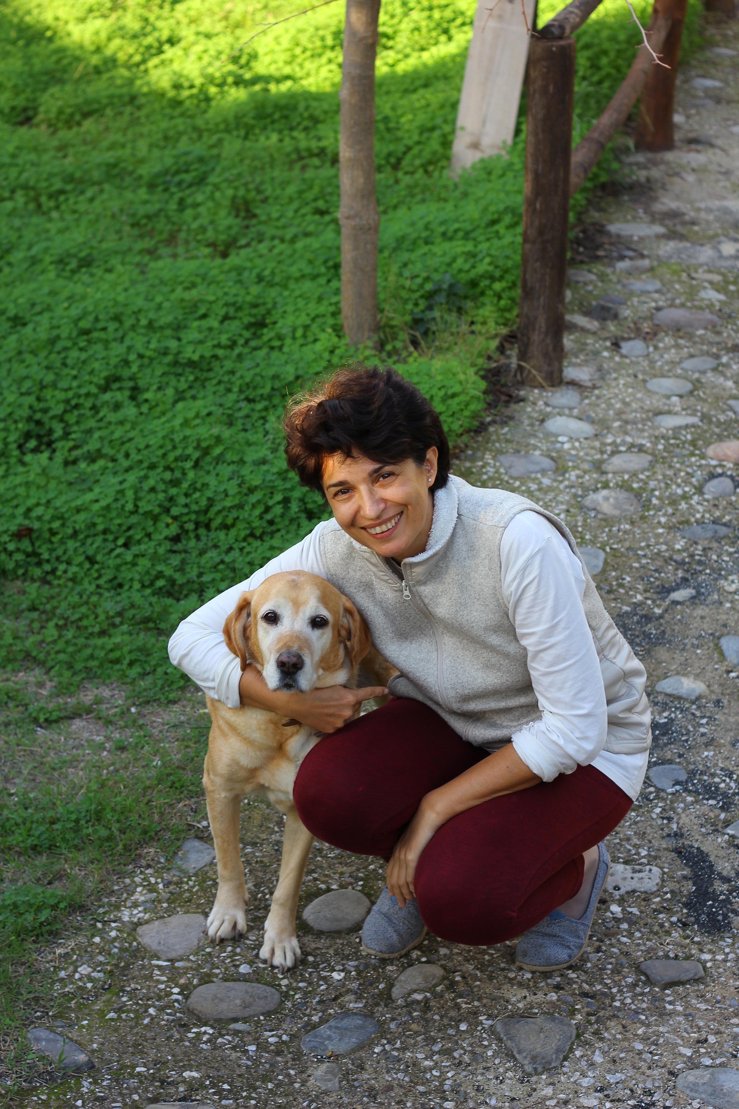 Illustrator Olena kneeling on a stone path outdoors, smiling and holding a yellow Labrador retriever dog.