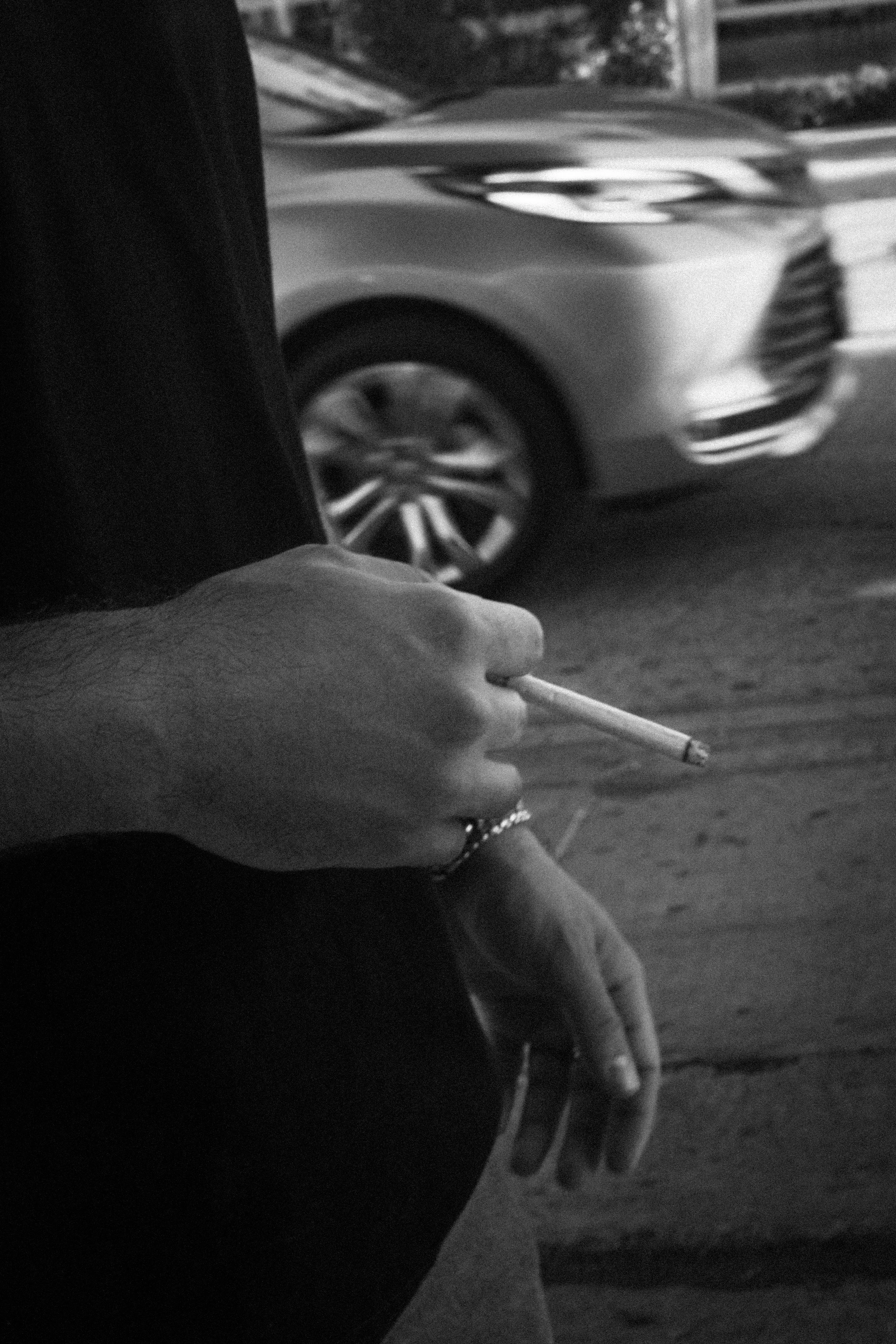 Black-and-white close-up of a person holding a lit cigarette over an ashtray.