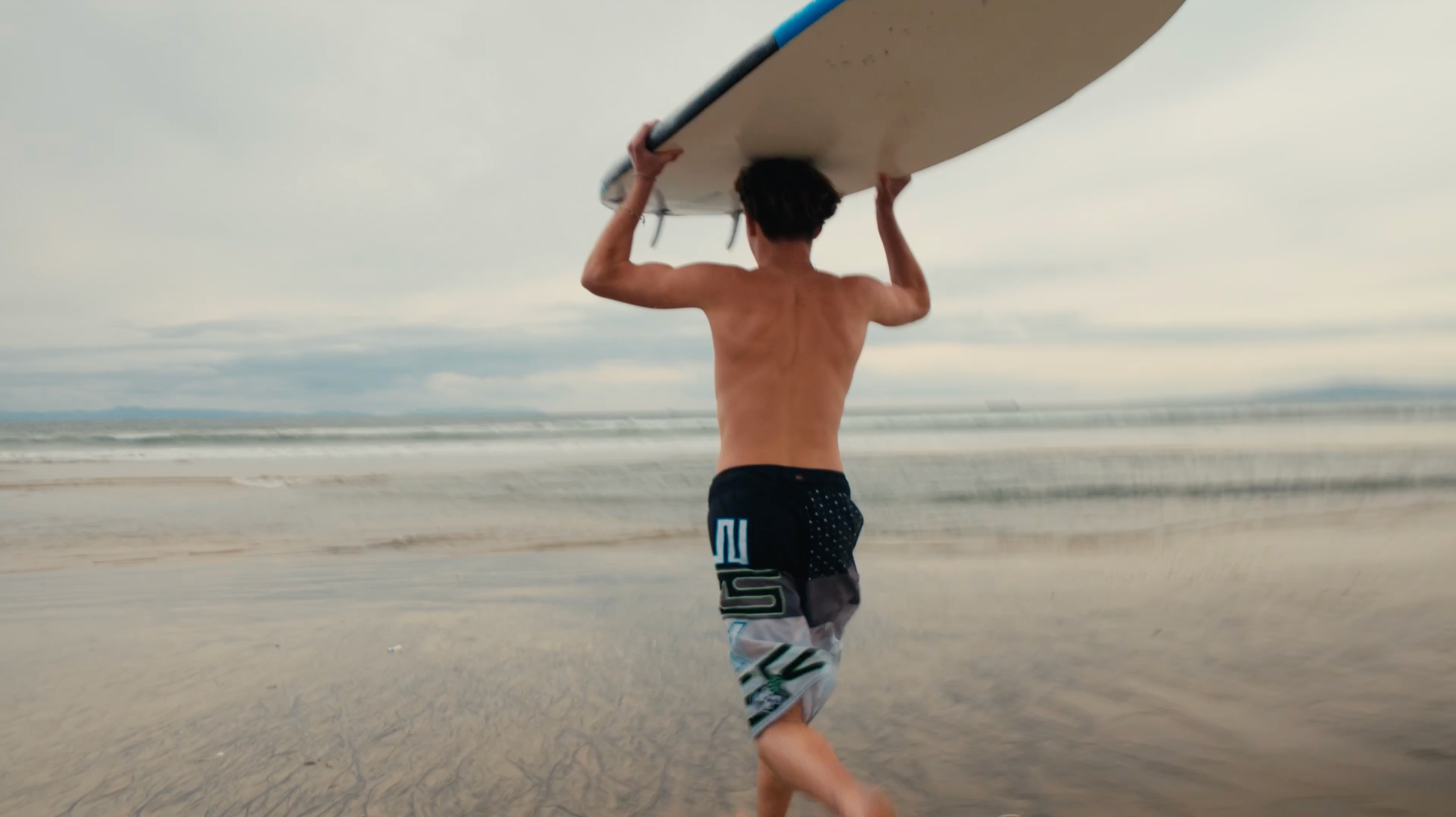 Surfer carrying a surfboard toward the ocean on a sandy beach