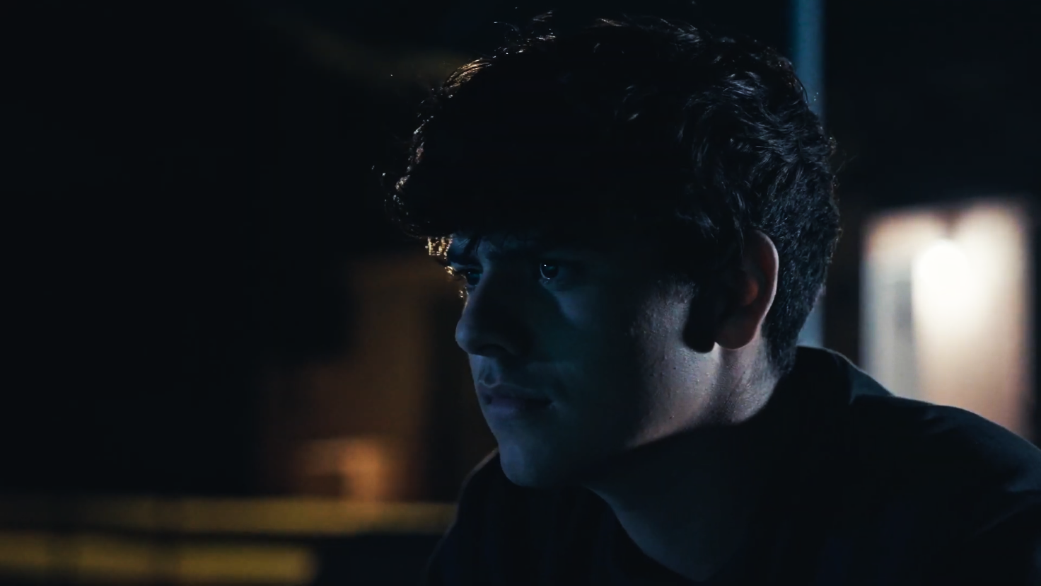 Close-up of a young man with curly hair in a dark, blue-lit room