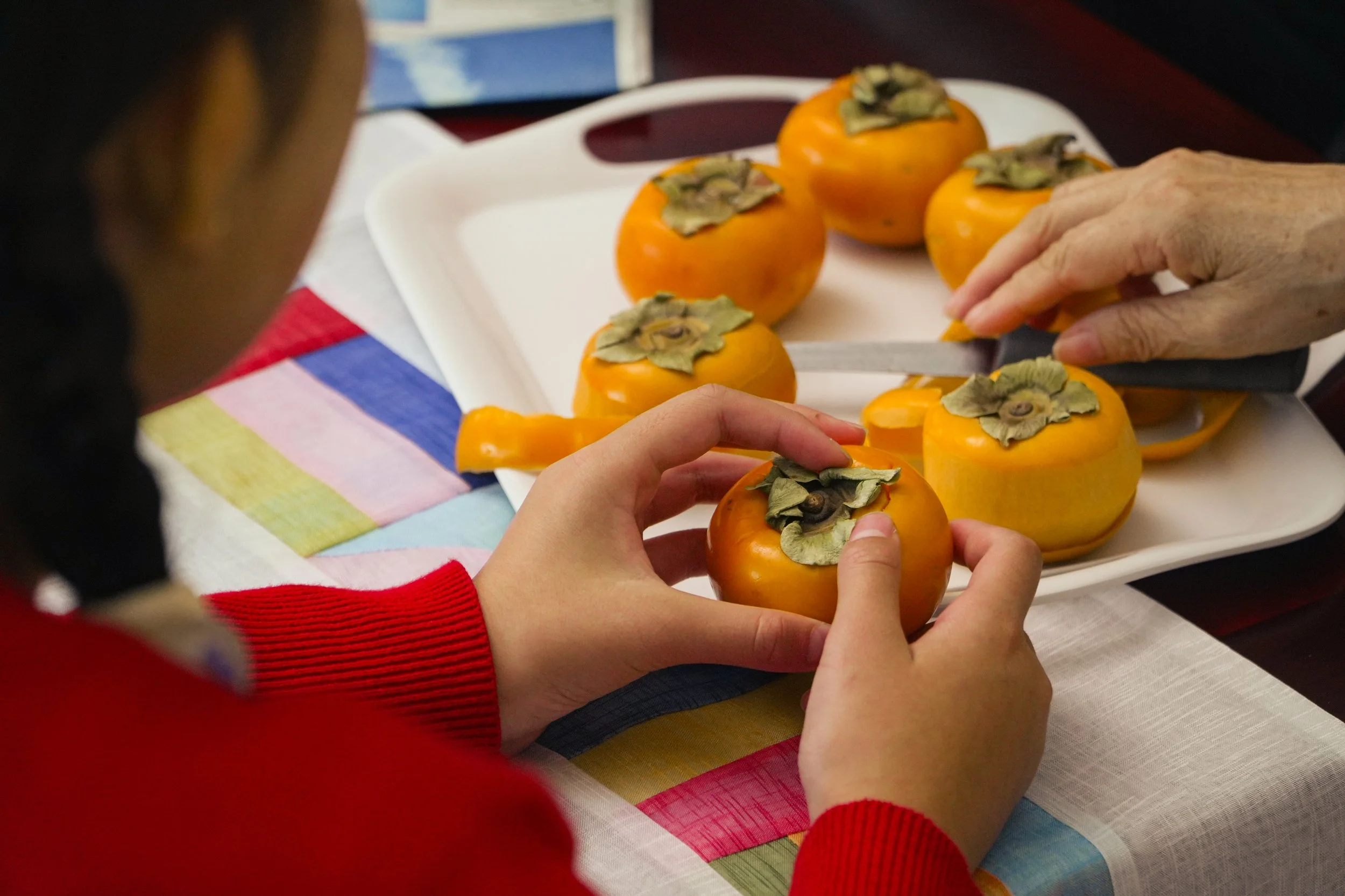 People slicing and preparing ripe persimmons on a white serving tray