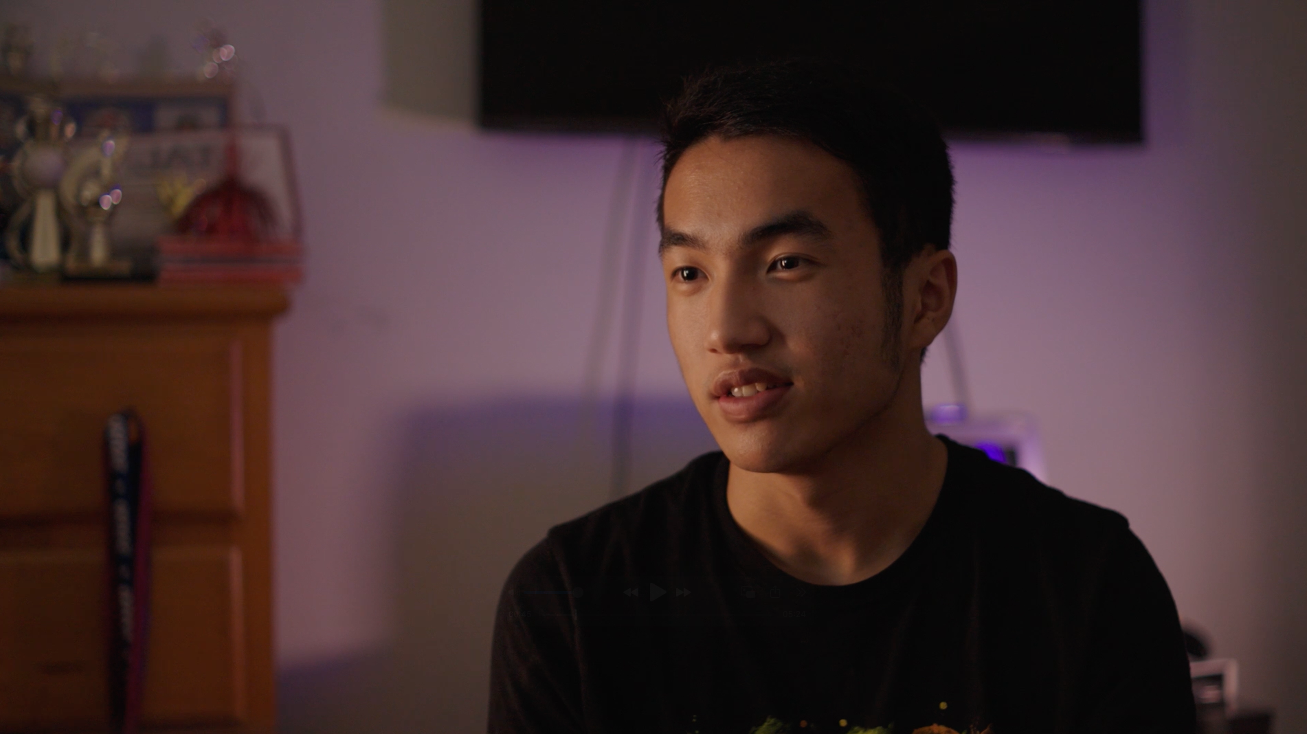 Young man in a black shirt sitting indoors in a dimly lit room