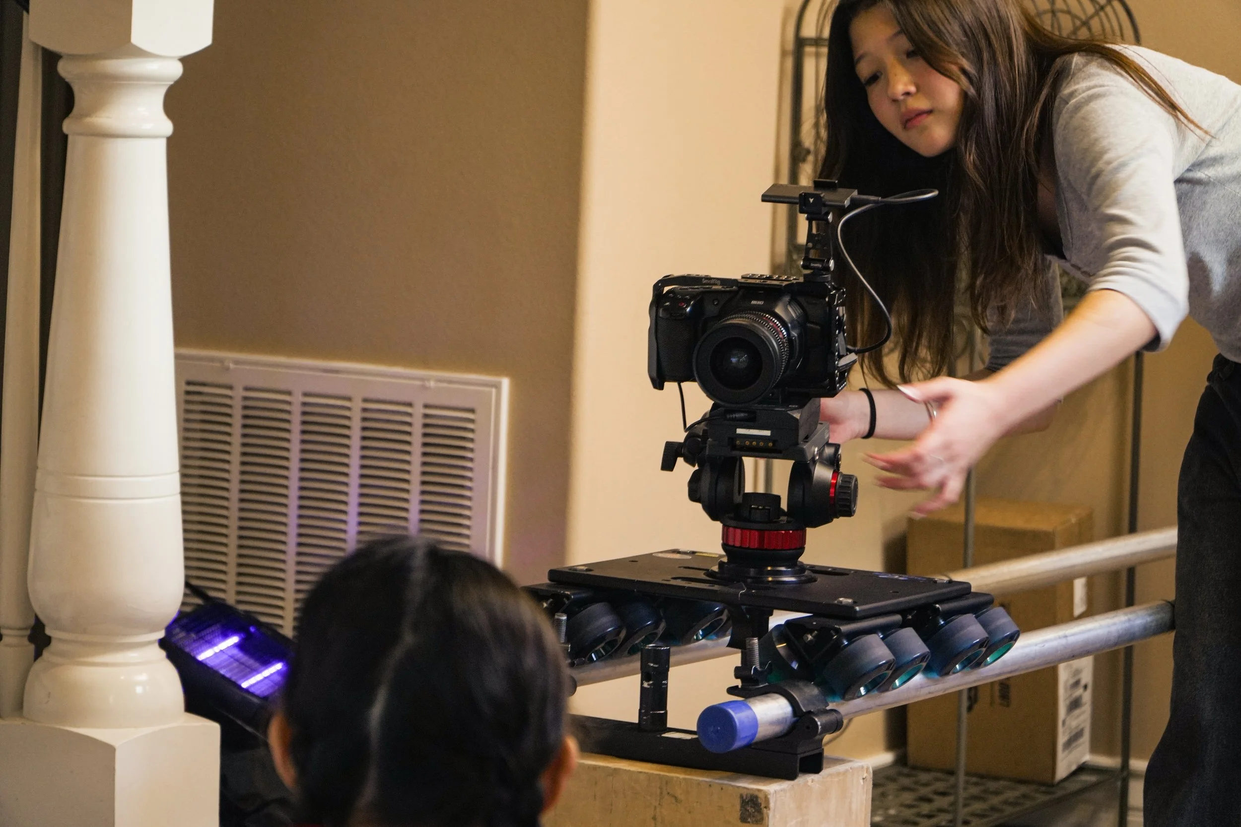 Woman operating a professional video camera mounted on a rolling dolly track indoors.