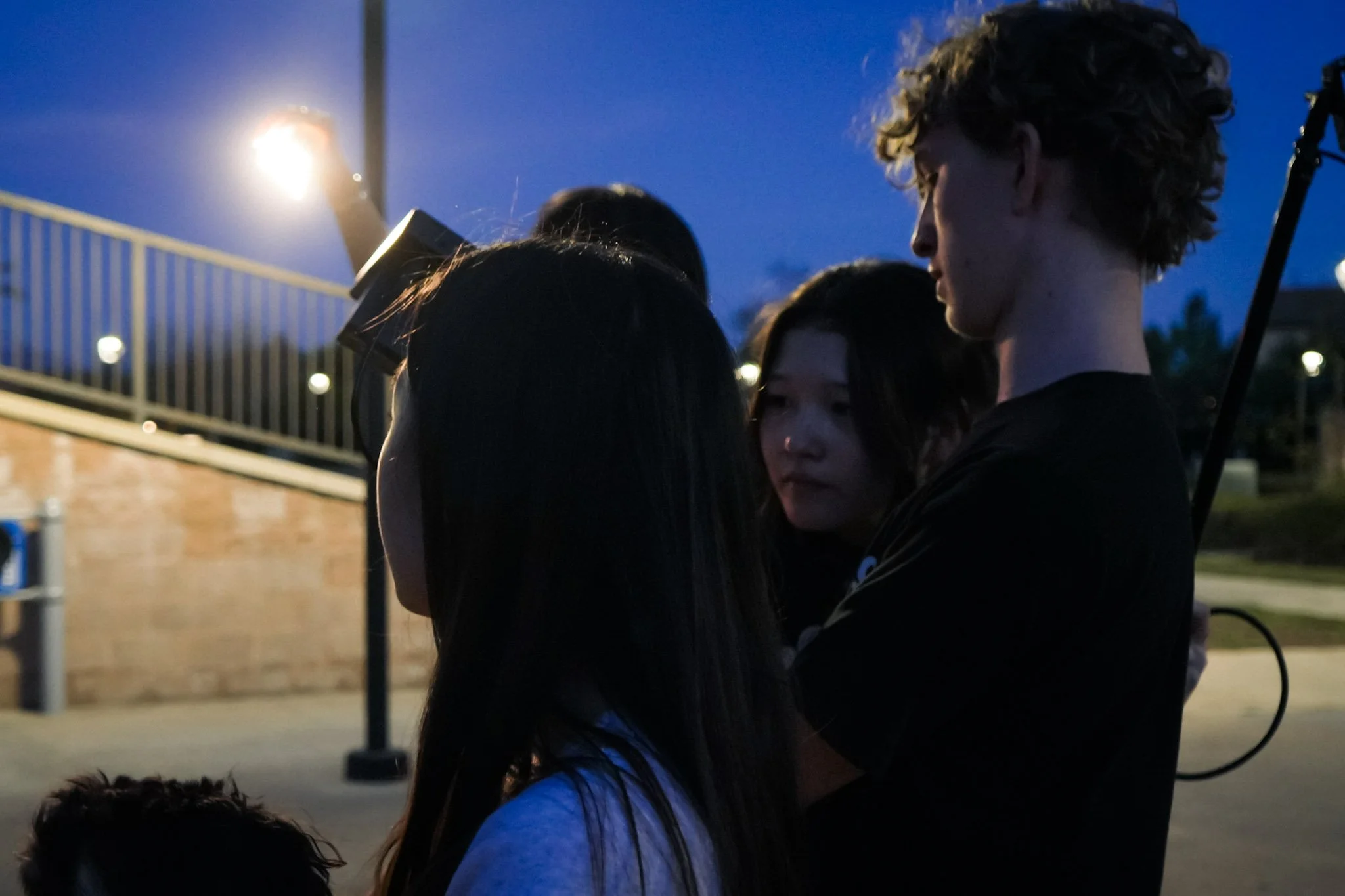 Group of people gathered outdoors at dusk near a lit sports court