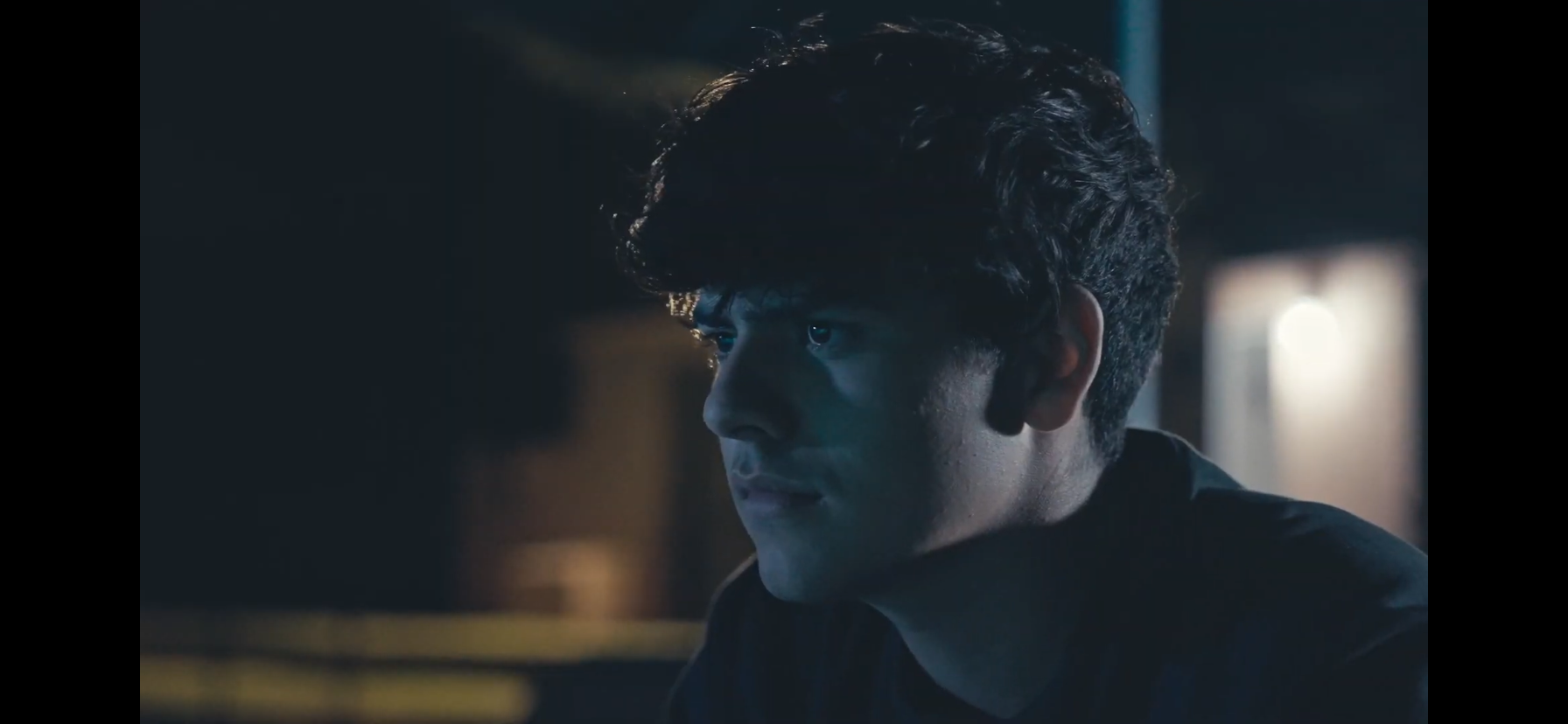 Close-up of a young man with curly dark hair in moody blue lighting indoors