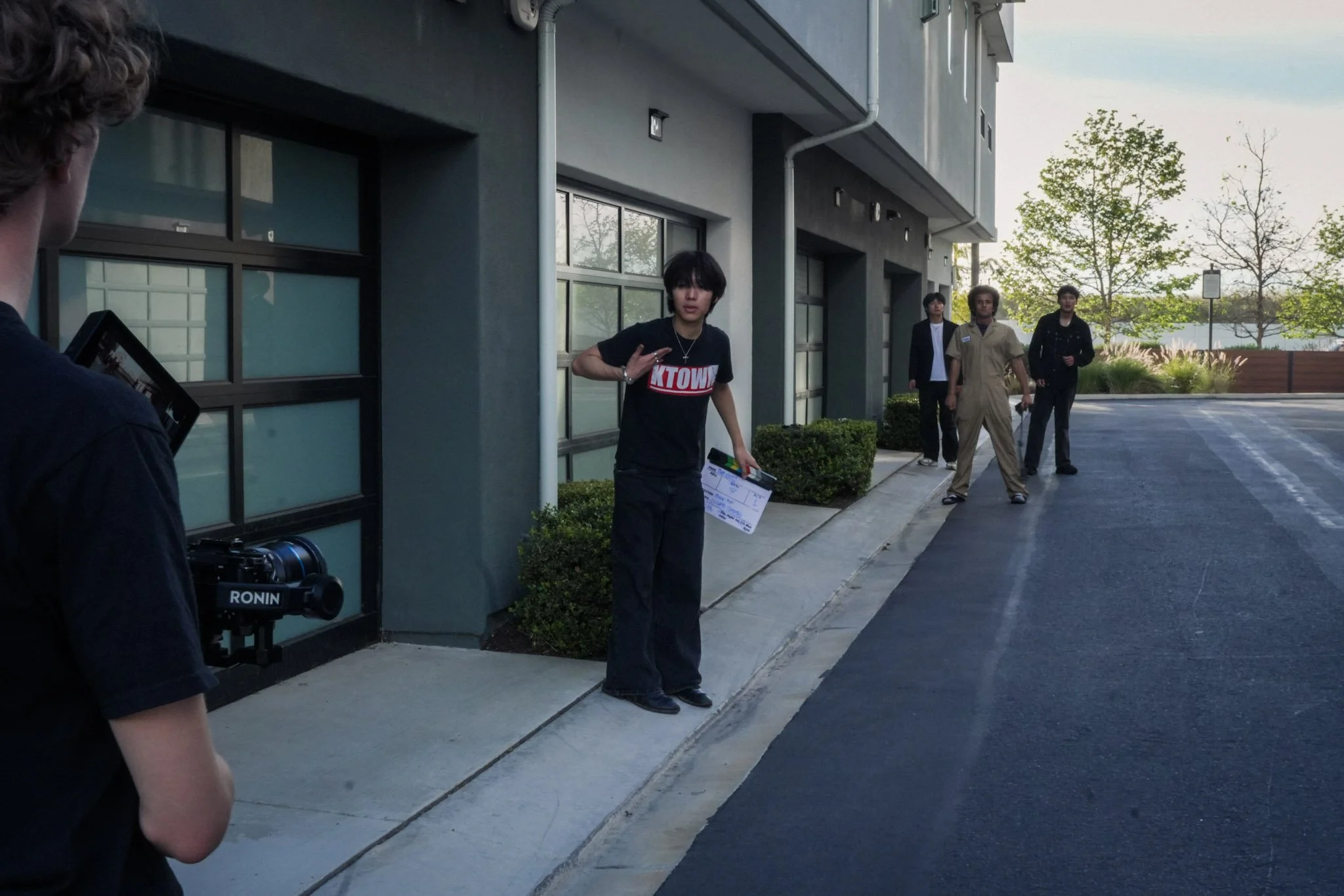 Group of young men filming outside a modern building, with a camera operator and clapperboard visible.