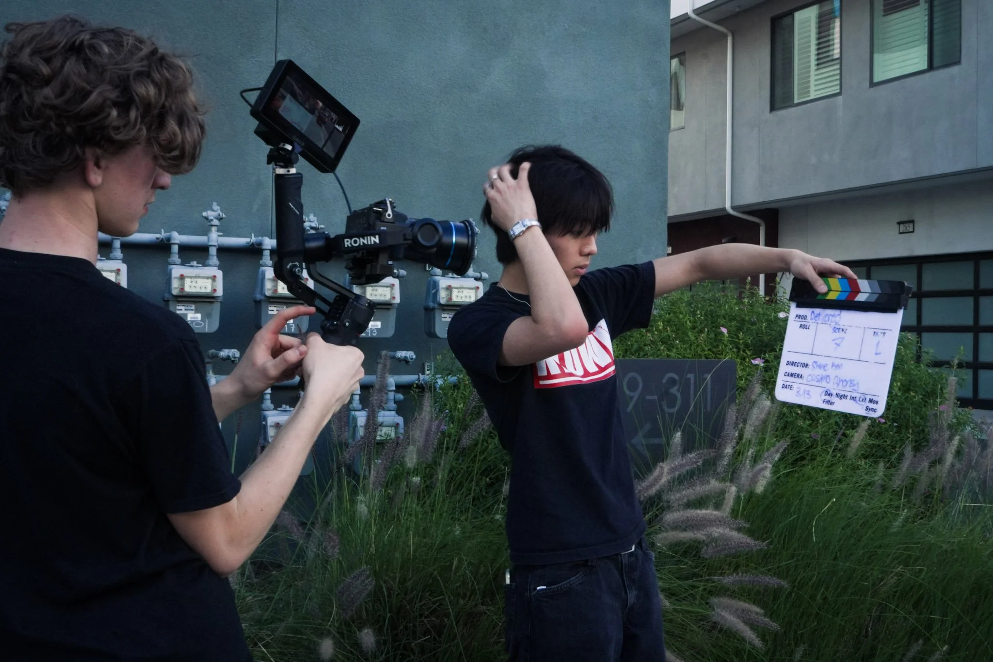 Film crew filming a young actor with a handheld camera rig and clapperboard outside a house