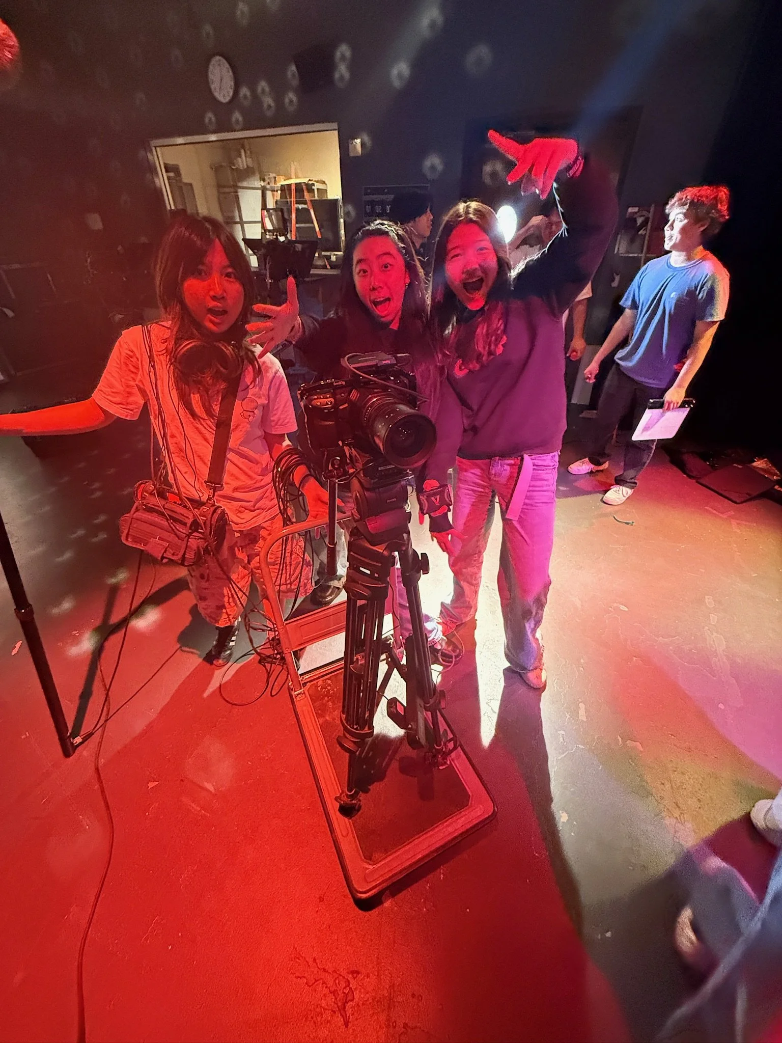 Excited film crew posing around a professional video camera on a dolly in a red-lit studio