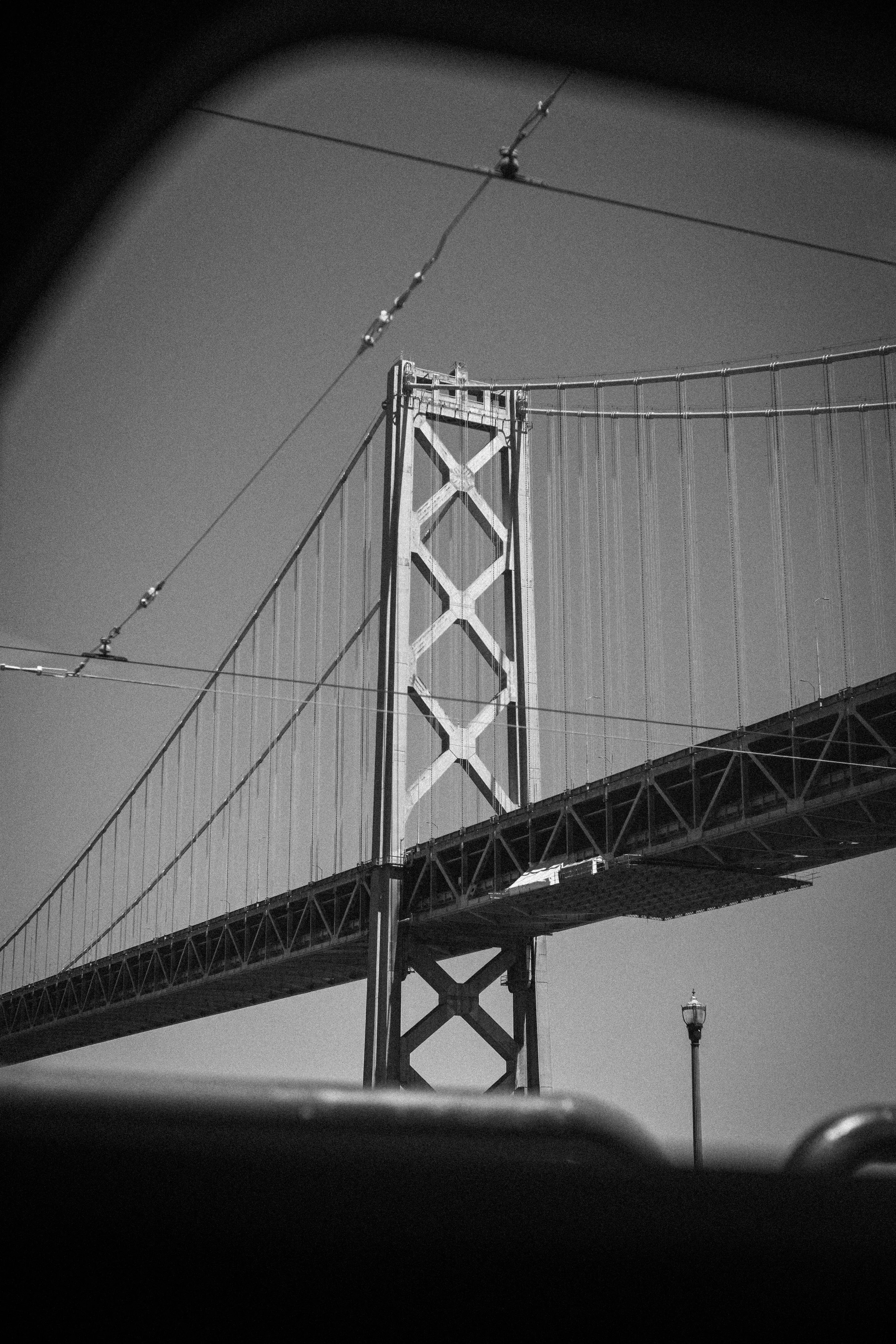 Black-and-white view of a suspension bridge tower, cables, and roadway from below