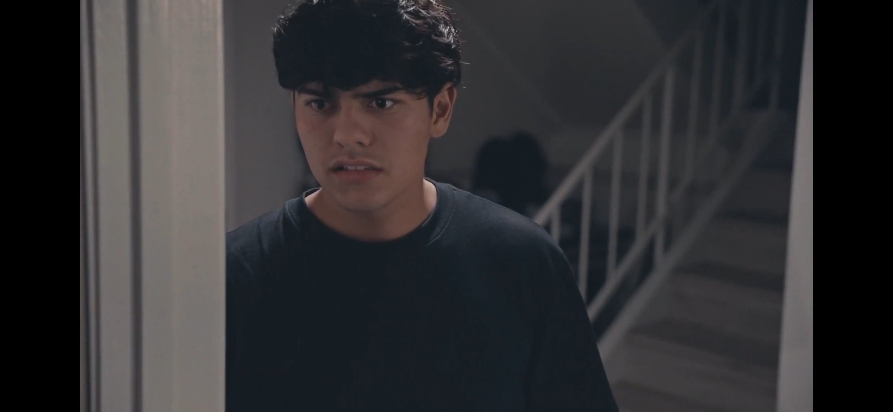 Concerned young man in a black shirt standing near a staircase indoors