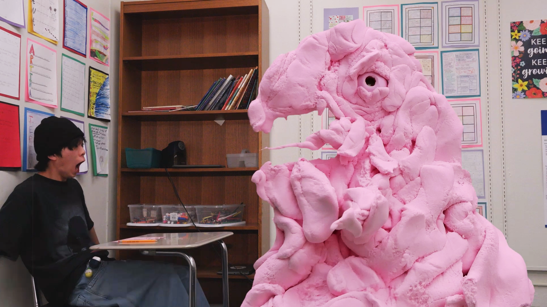 Person reacting in surprise to a large pink bird-like monster costume in a classroom