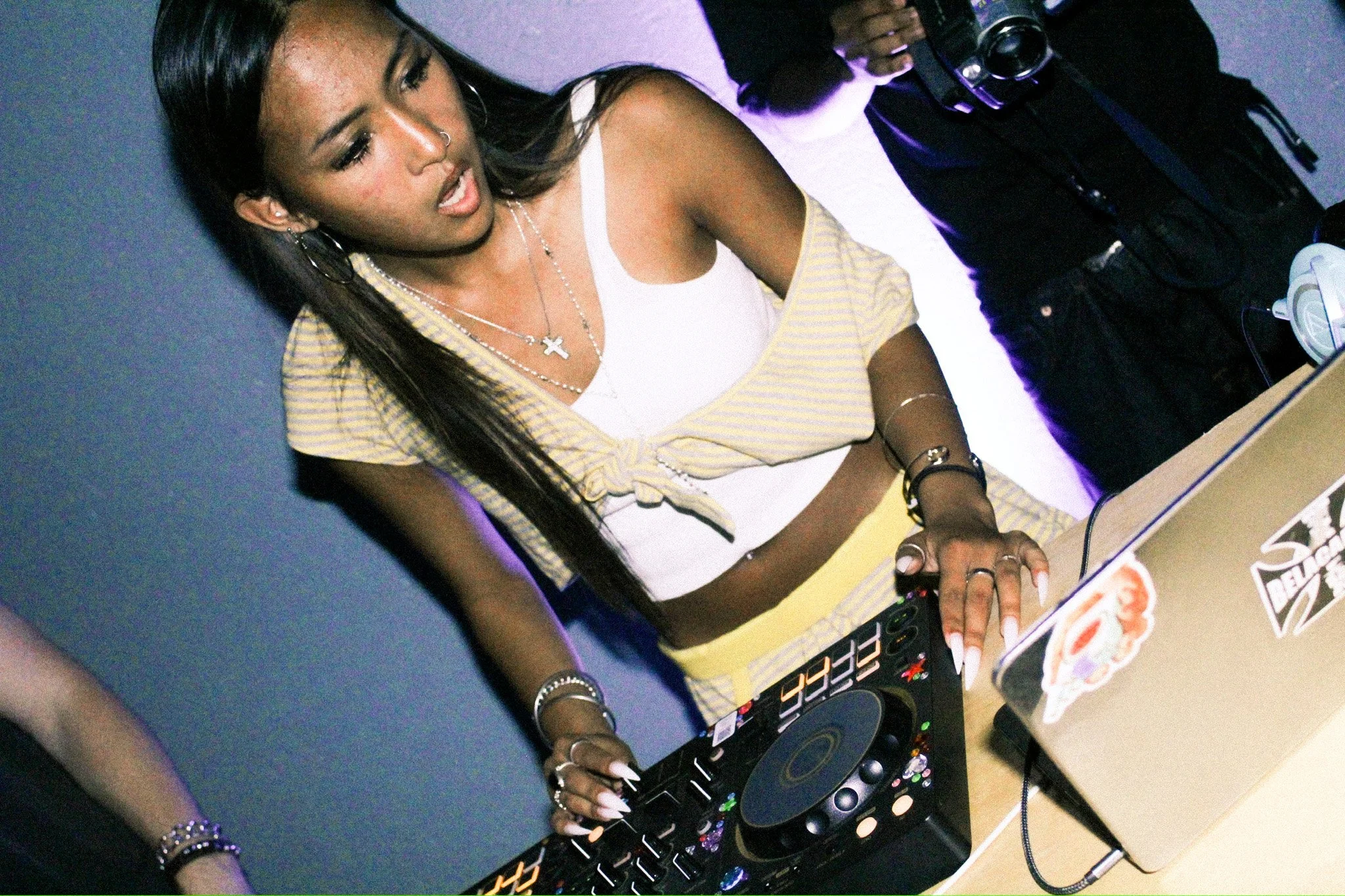 Woman operating a DJ controller beside a laptop at a club or party