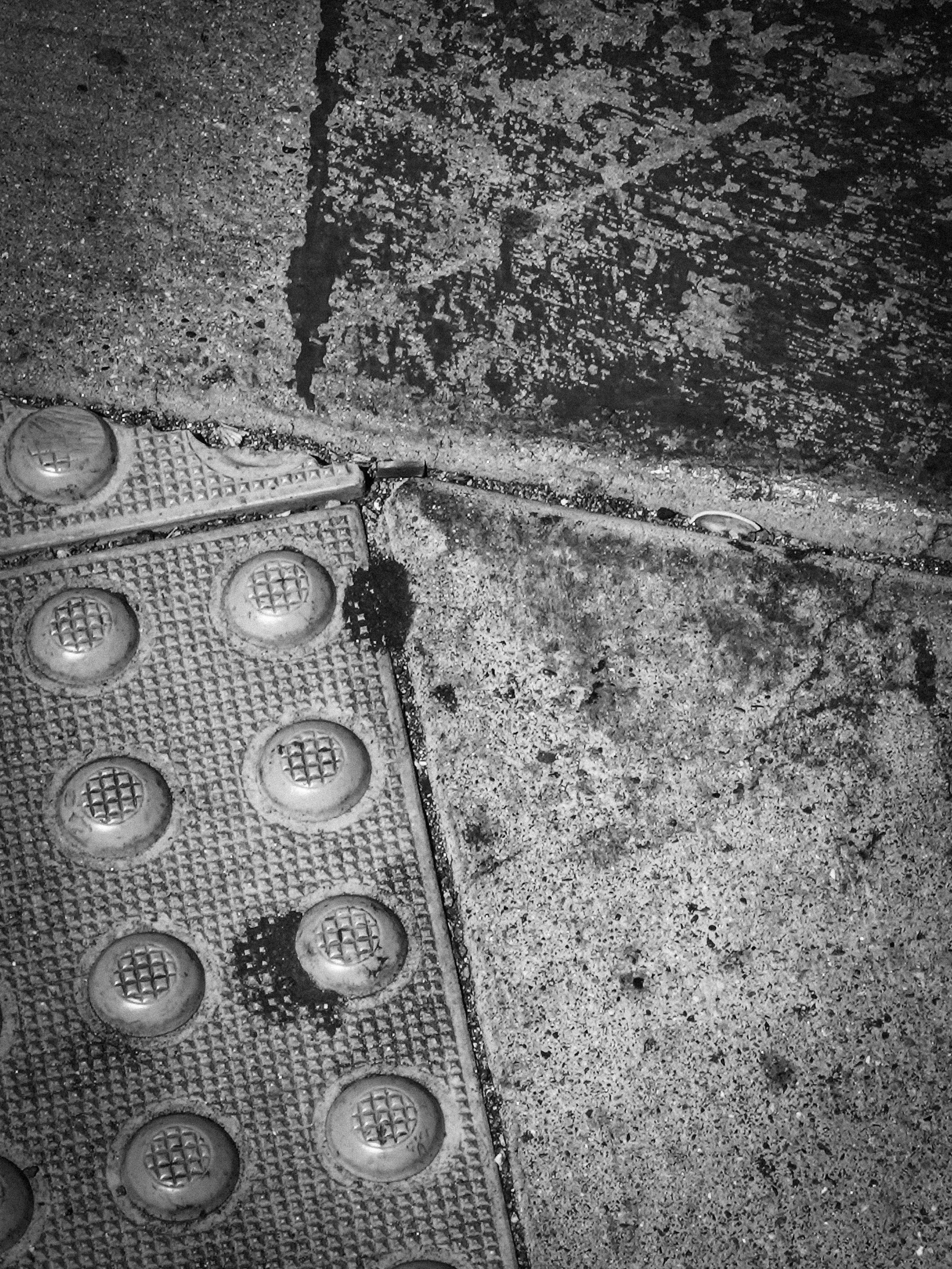 Close-up black-and-white photo of textured rubber soles with round tread lugs on rough pavement.