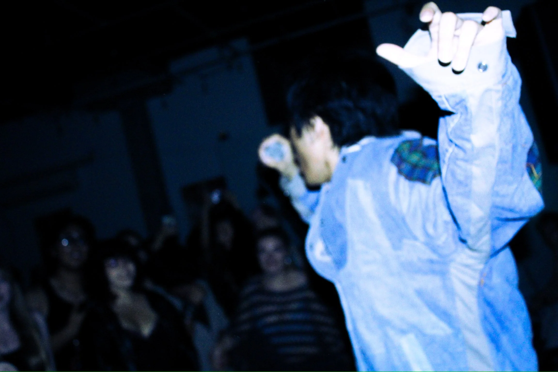 Person in a white protective suit and gloves raising a hand in a dark crowd